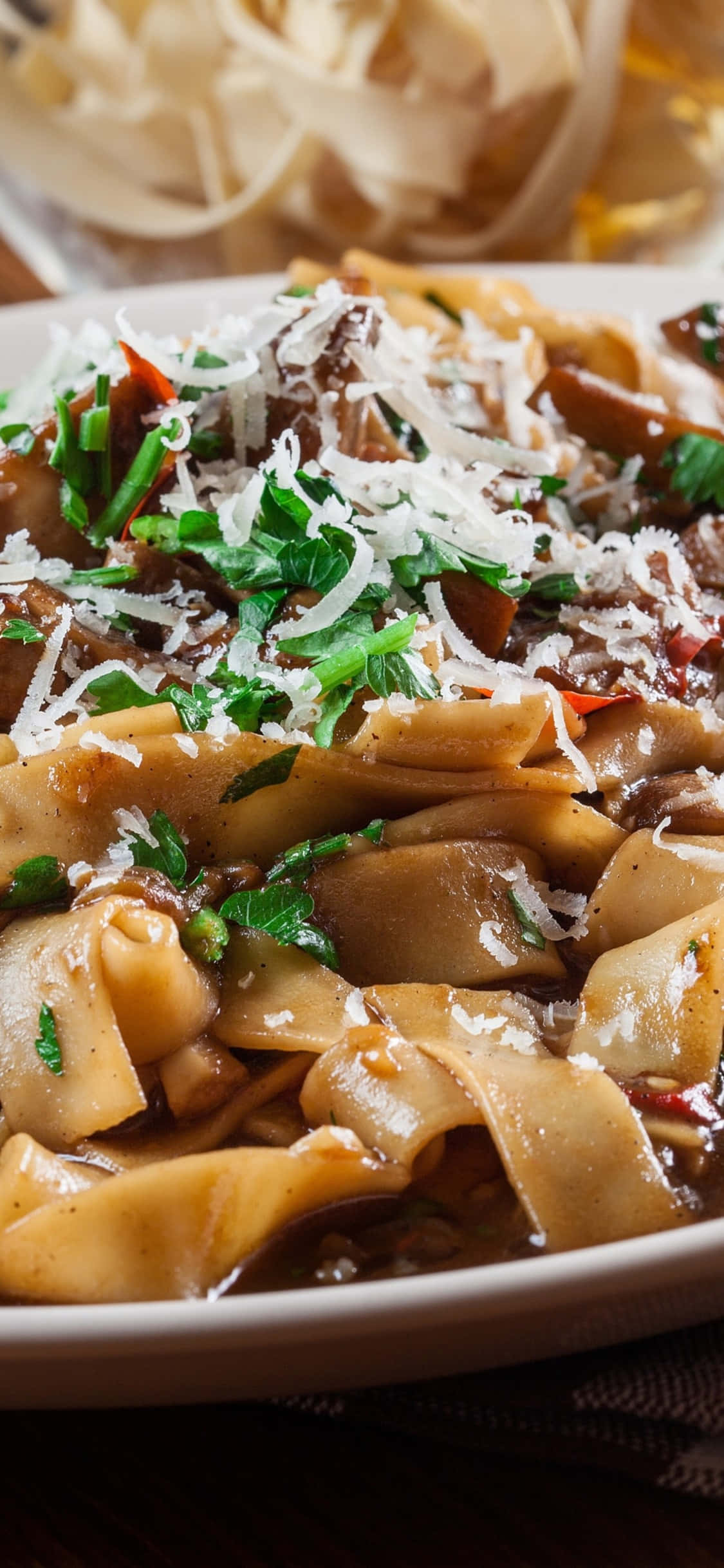 iPhone X Pasta 桌布 壁紙 — 寬條義大利麵搭配濃郁醬汁的特寫，上面撒上新鮮歐芹和磨碎的起司。