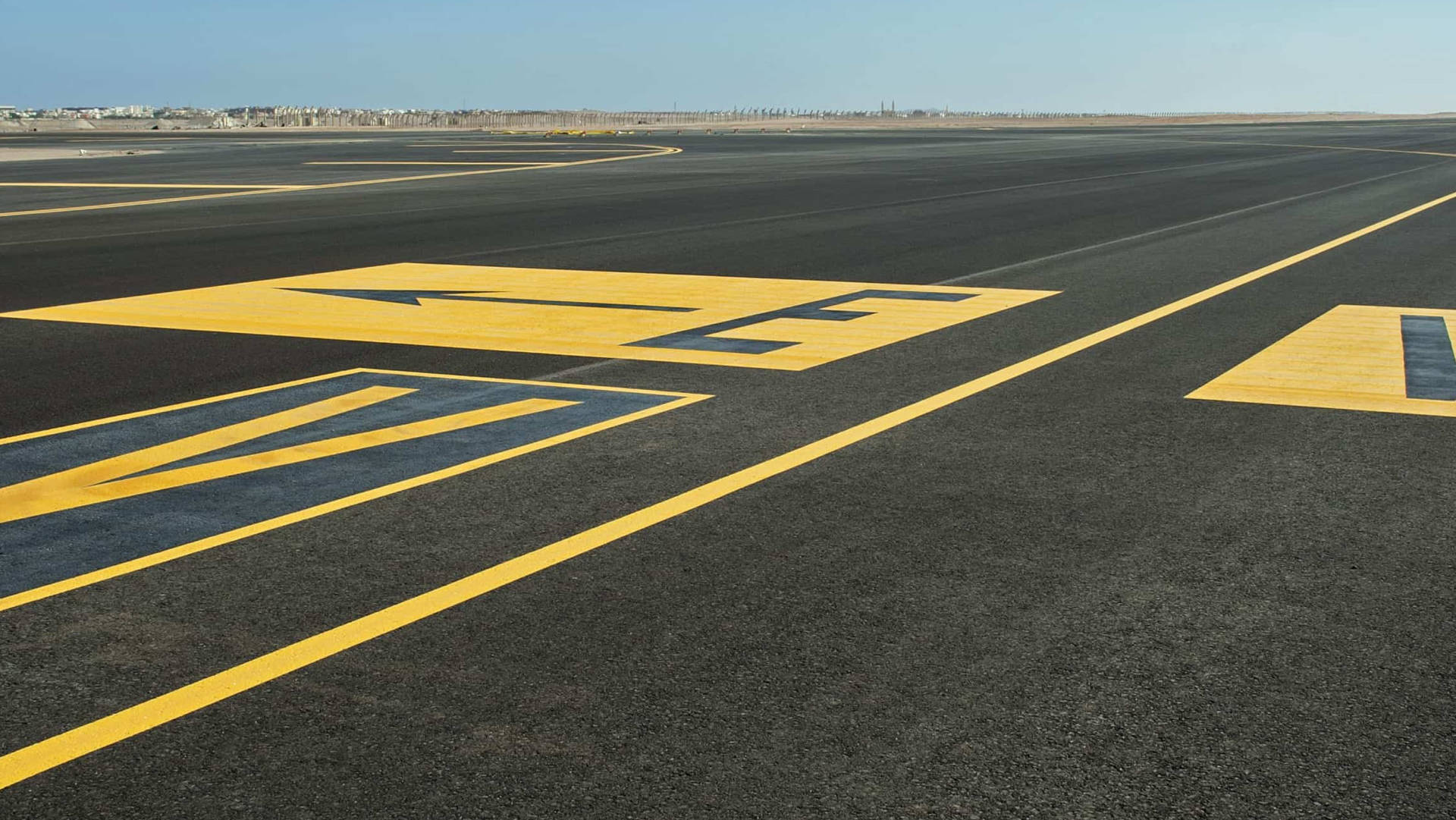 Runway 桌布 壁紙 — 寬闊的機場跑道，帶有粗體黃色方向箭頭和線條，在晴朗的藍天下。