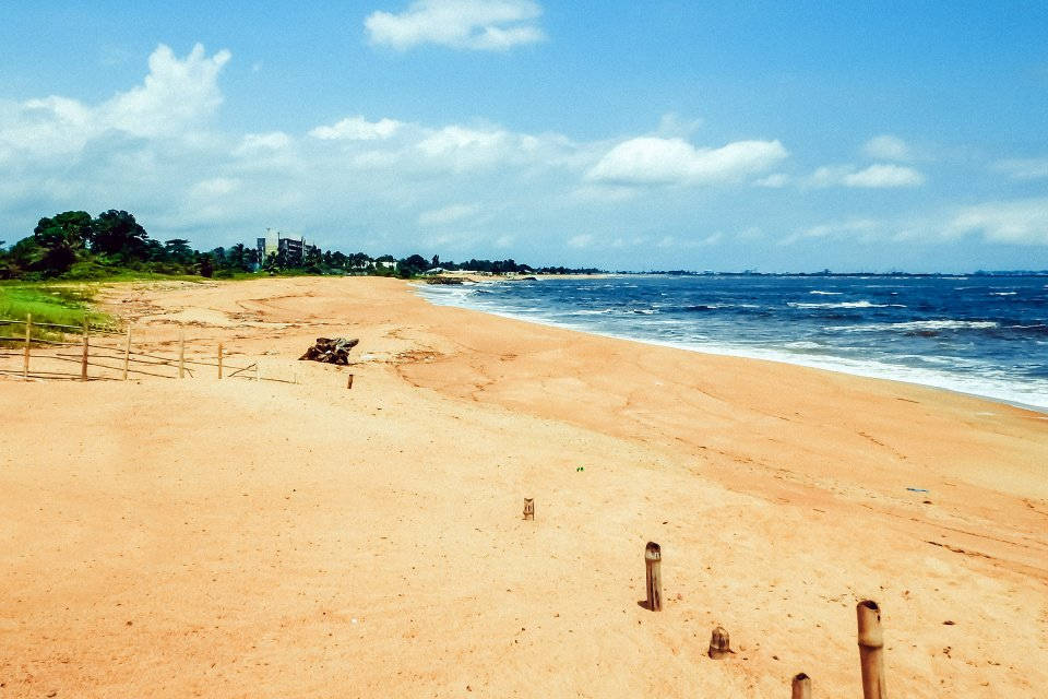 Liberia 桌布 壁紙 — 寬闊的沙灘在明亮的藍天下延伸， fluffy 雲朵點綴，溫柔的海浪拍打著海岸。