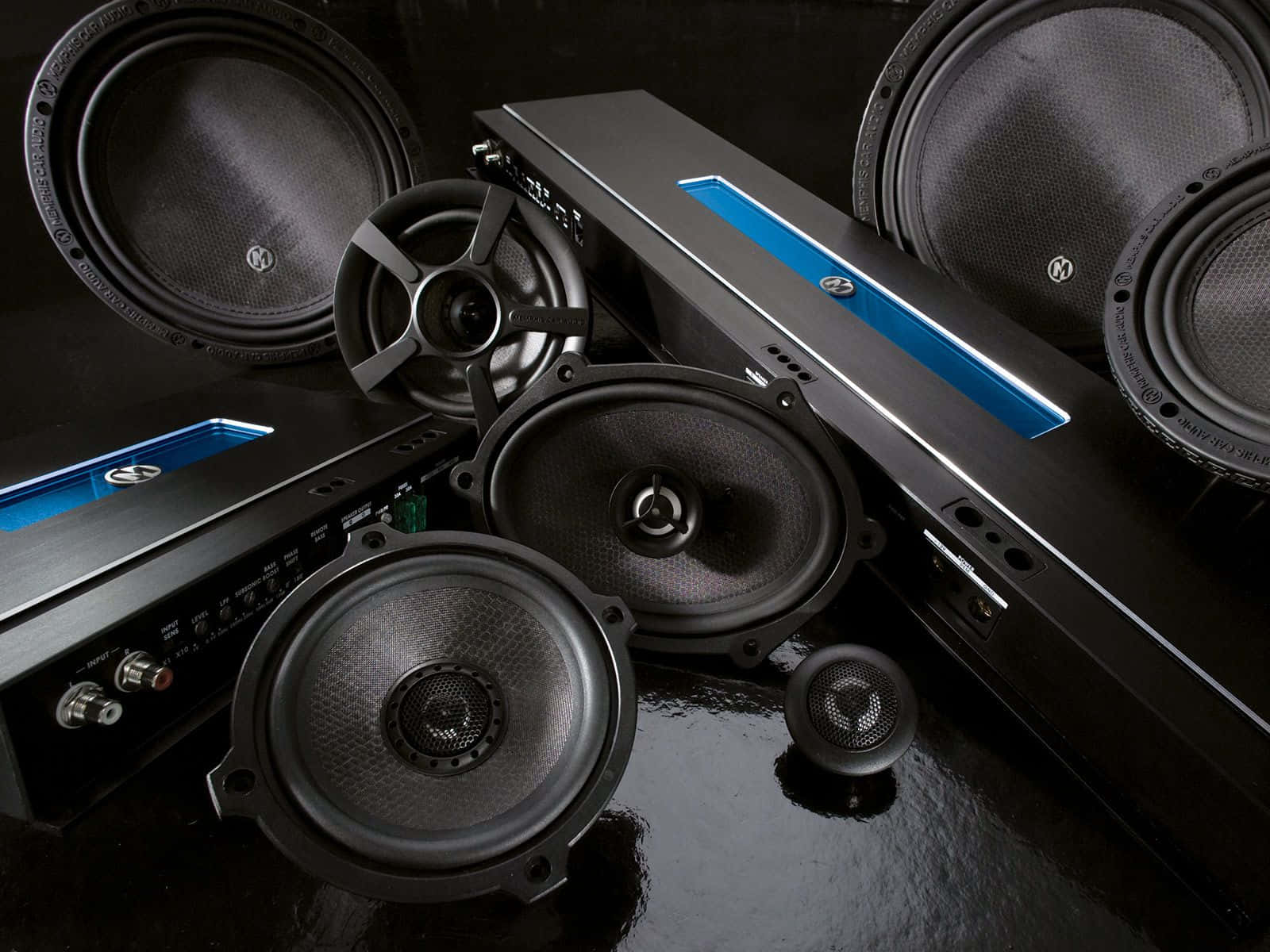 Car Audio 桌布 壁紙 — 專業汽車音響組件，包括揚聲器和放大器，排列在帶有藍色重點照明的光澤黑色表面上。