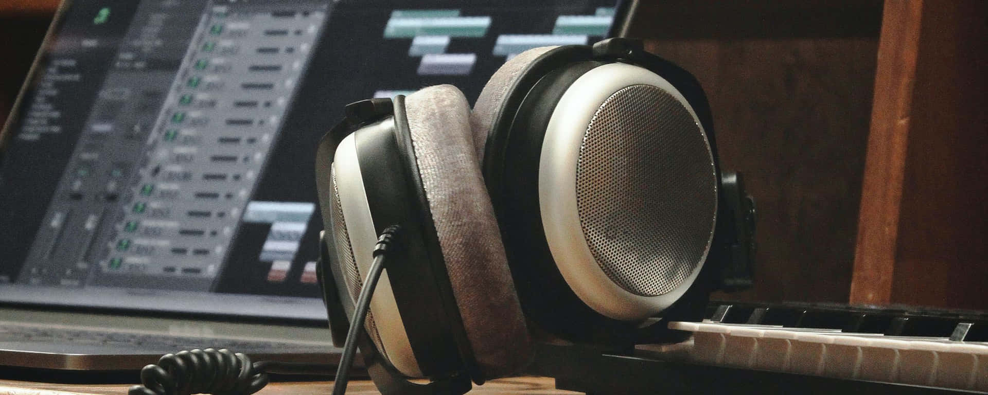 桌布 壁紙 — 專業錄音室耳機放在鋼琴鍵盤上，旁邊是顯示音頻編輯軟體的筆記型電腦。