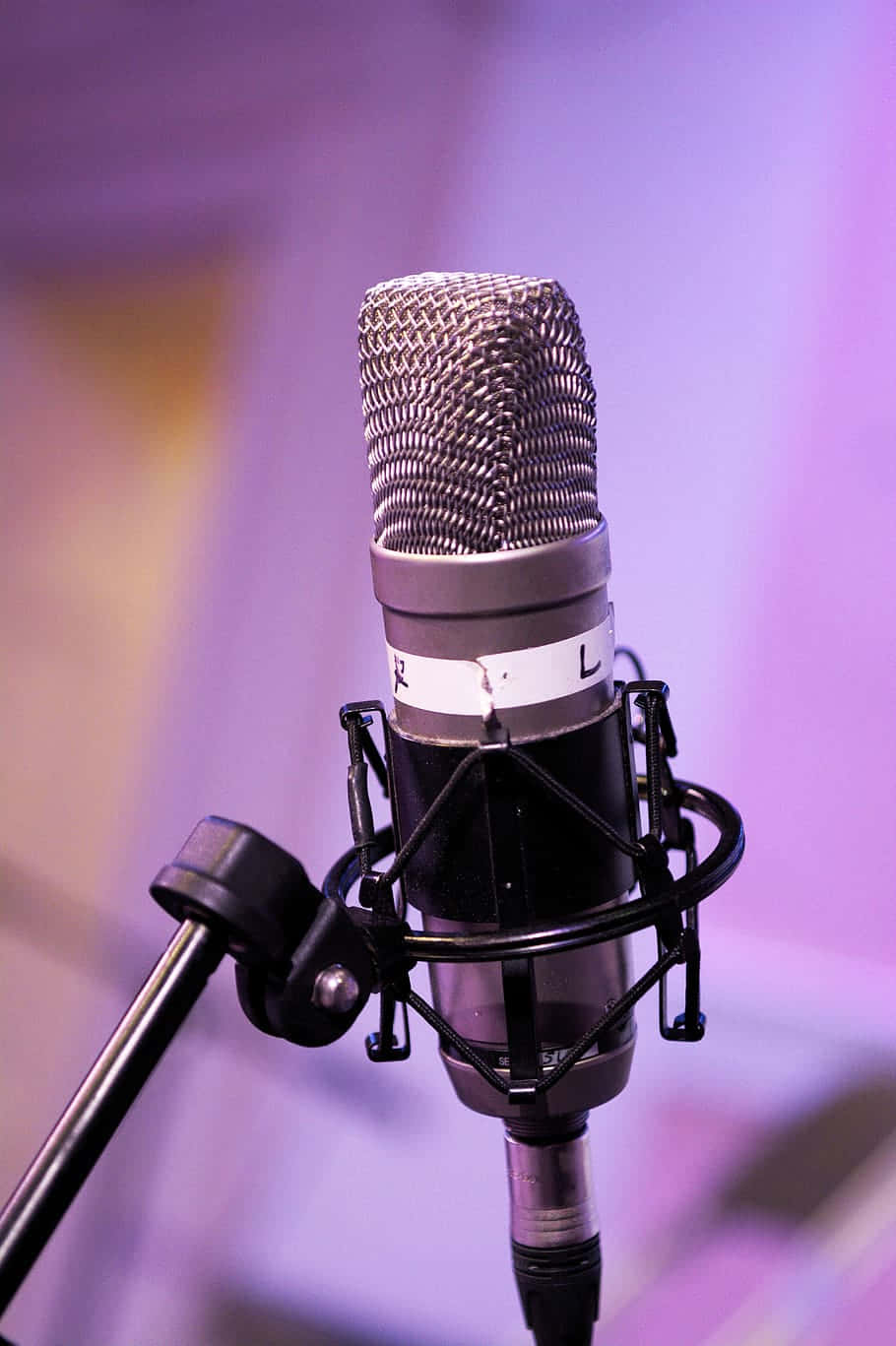 Sound 桌布 壁紙 — 專業錄音室麥克風的特寫，帶有金屬網罩和防震架，背景為柔和的紫色。