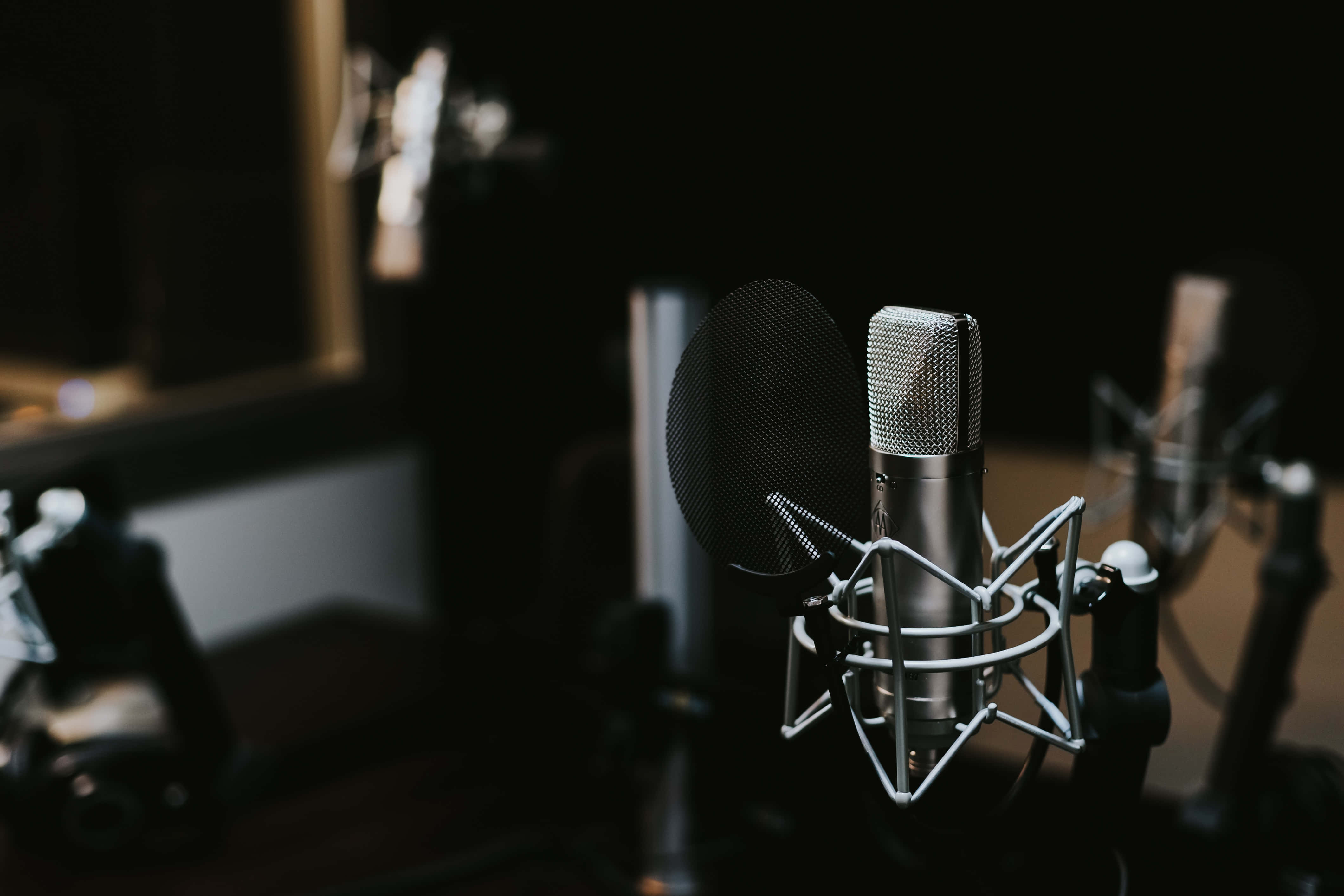 recording 桌布 壁紙 — 專業錄音室麥克風配備防噴罩和防震架，在黑暗模糊的背景中清晰對焦。
