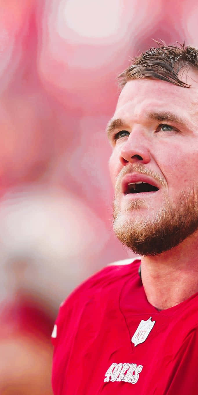 Mike Mcglinchey 桌布 壁紙 — 專注的NFL球員身穿紅色49ers球衣的特寫，背景是模糊的球場燈光。