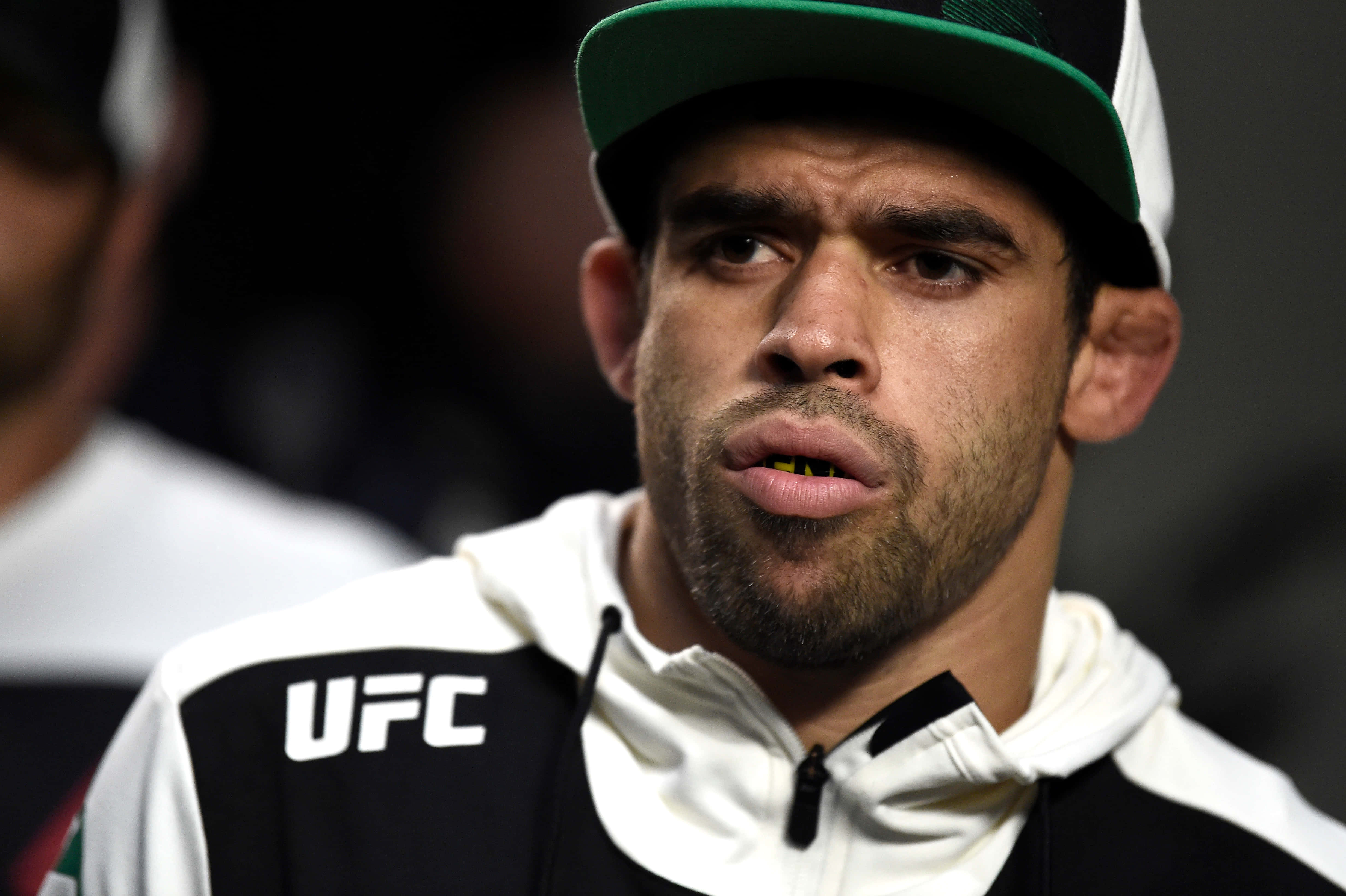 UFC 桌布 壁紙 — 專注的UFC拳手特寫，戴著綠色和白色帽子及品牌連帽衫，背景深色。