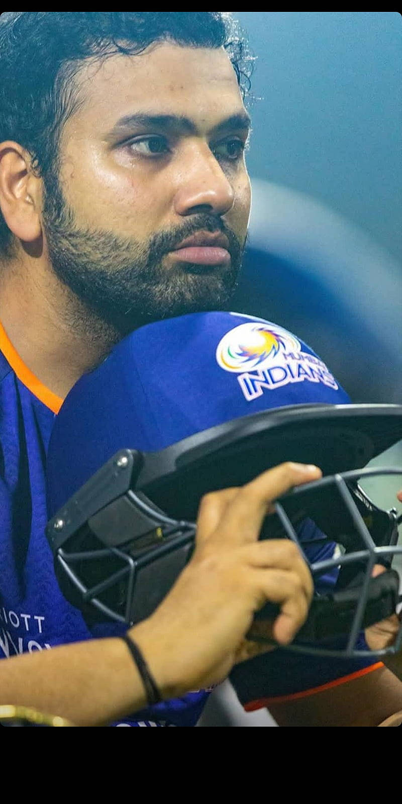 Mumbai Indians 桌布 壁紙 — 專注的板球運動員在體育場燈光下手持帶有'INDIANS'標誌的藍色頭盔的特寫。