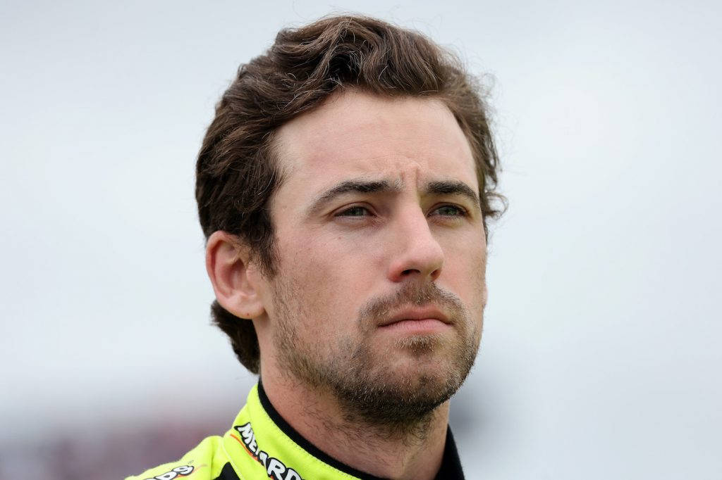 Ryan Blaney 桌布 壁紙 — 專注的男性賽車手穿著亮黃色賽車服的近距離肖像，背景為柔和的灰色。