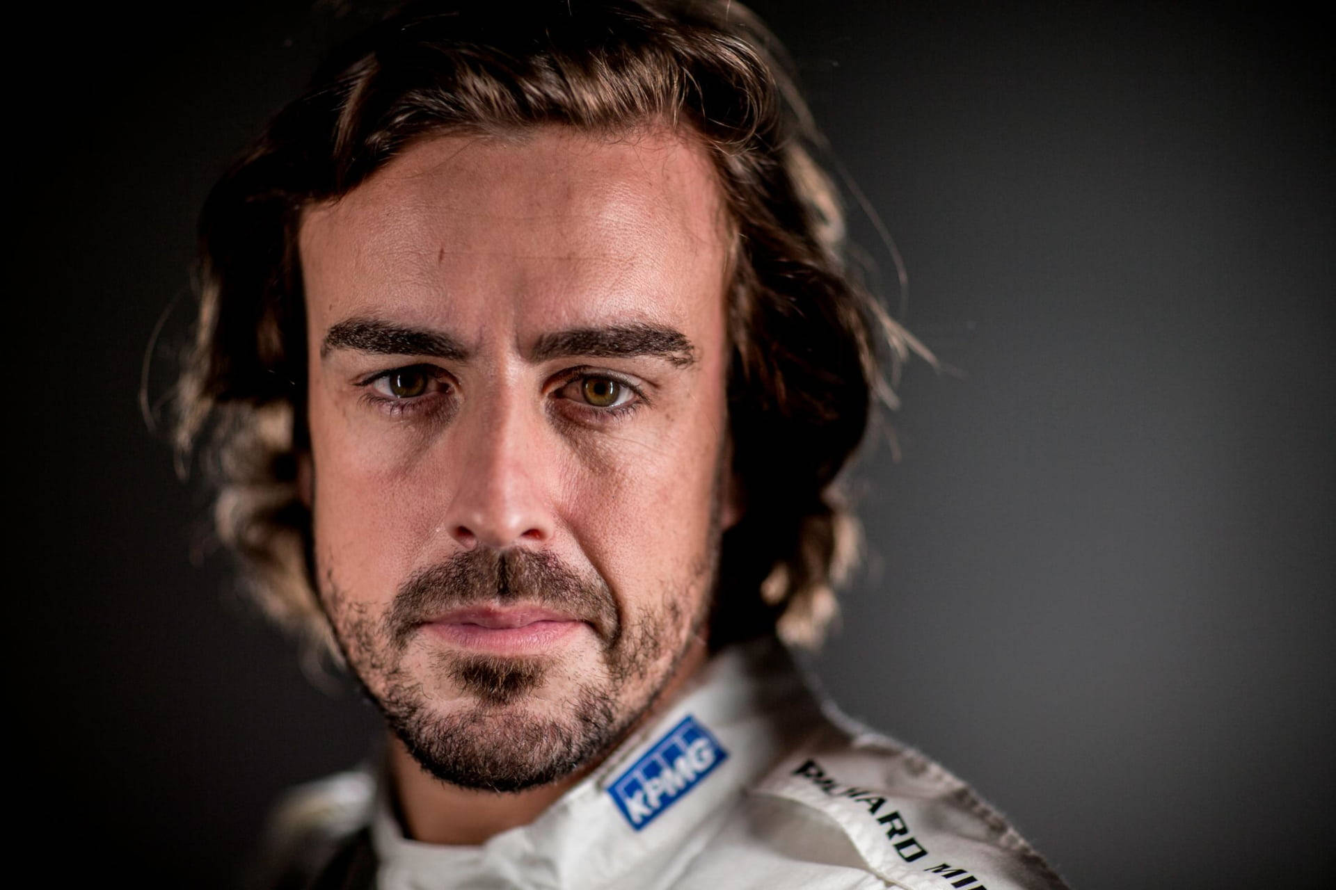 Fernando Alonso 桌布 壁紙 — 專注的男性賽車手穿著白色賽車服，在深色漸變背景下的特寫肖像。