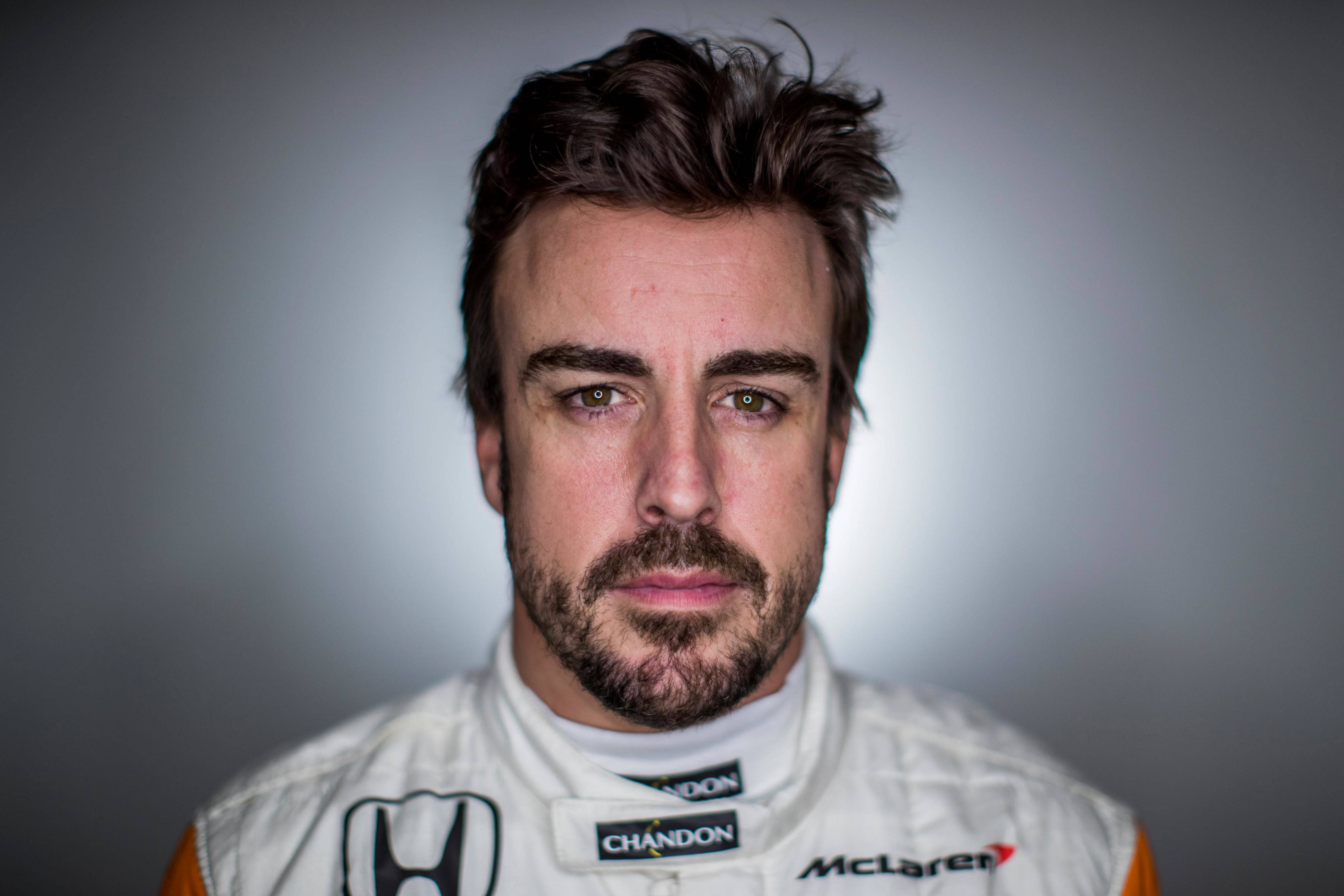 Fernando Alonso 桌布 壁紙 — 專注的男性賽車手身穿白色McLaren賽車服的近距離肖像，背景為柔和灰色漸變。