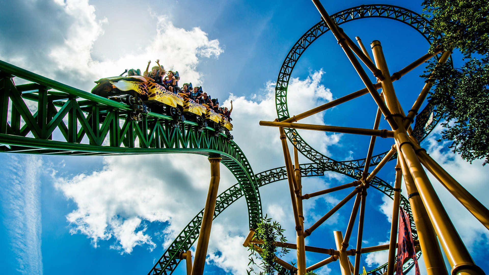 Roller Coaster 桌布 壁紙 — 尋求刺激的人們歡呼尖叫，一輛黃色雲霄飛車在綠色軌道上飛馳，背景是湛藍的天空和蓬鬆的白雲。