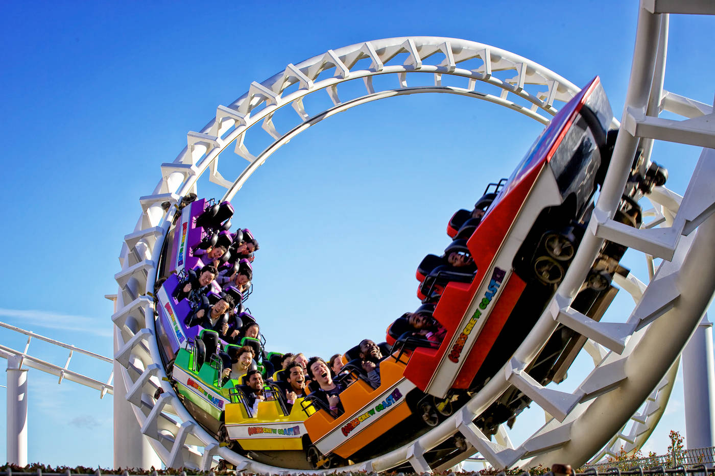 Roller Coaster 桌布 壁紙 — 尋求刺激的人在彩虹色的雲霄飛車在晴朗的藍天下倒轉翻滾時，興奮地尖叫。