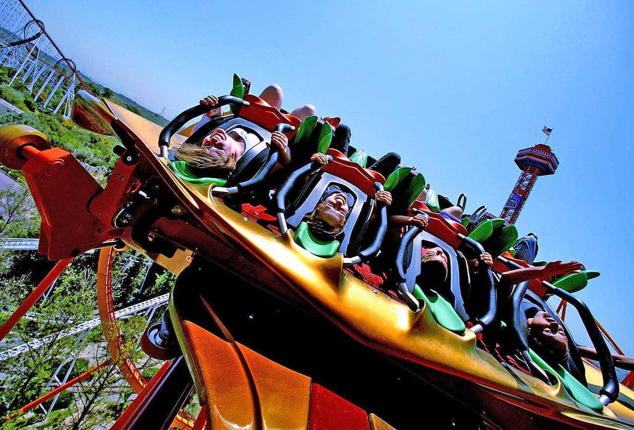 Six Flags 桌布 壁紙 — 尋求刺激的人在色彩繽紛的雲霄飛車車廂在清澈的藍天下倒掛疾馳時，興奮地尖叫。