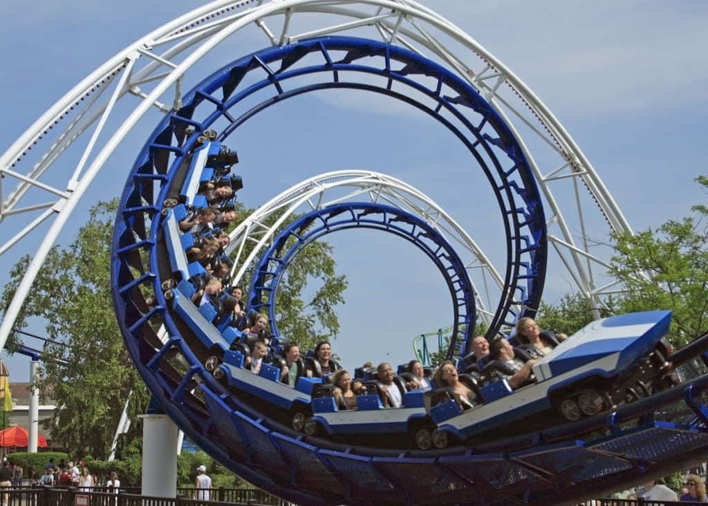 Roller Coaster 桌布 壁紙 — 尋求刺激的人在藍天白雲下尖叫，藍白相間的雲霄飛車在令人眩暈的螺旋中扭轉。