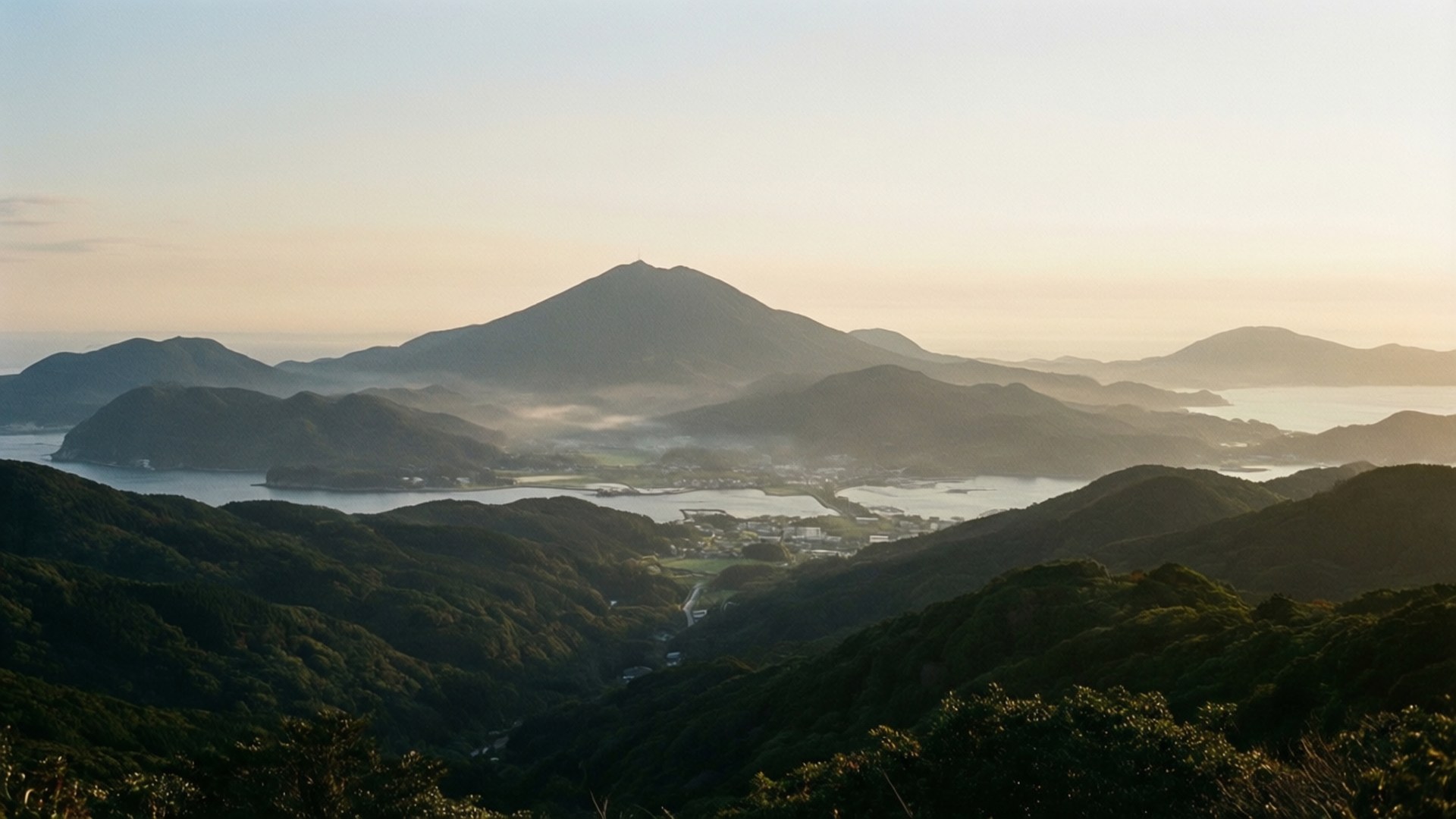 對馬島 壁紙 — 日出將層層疊疊的山脈和沿海海灣沐浴在溫暖的金色光芒中，薄霧籠罩著山谷。