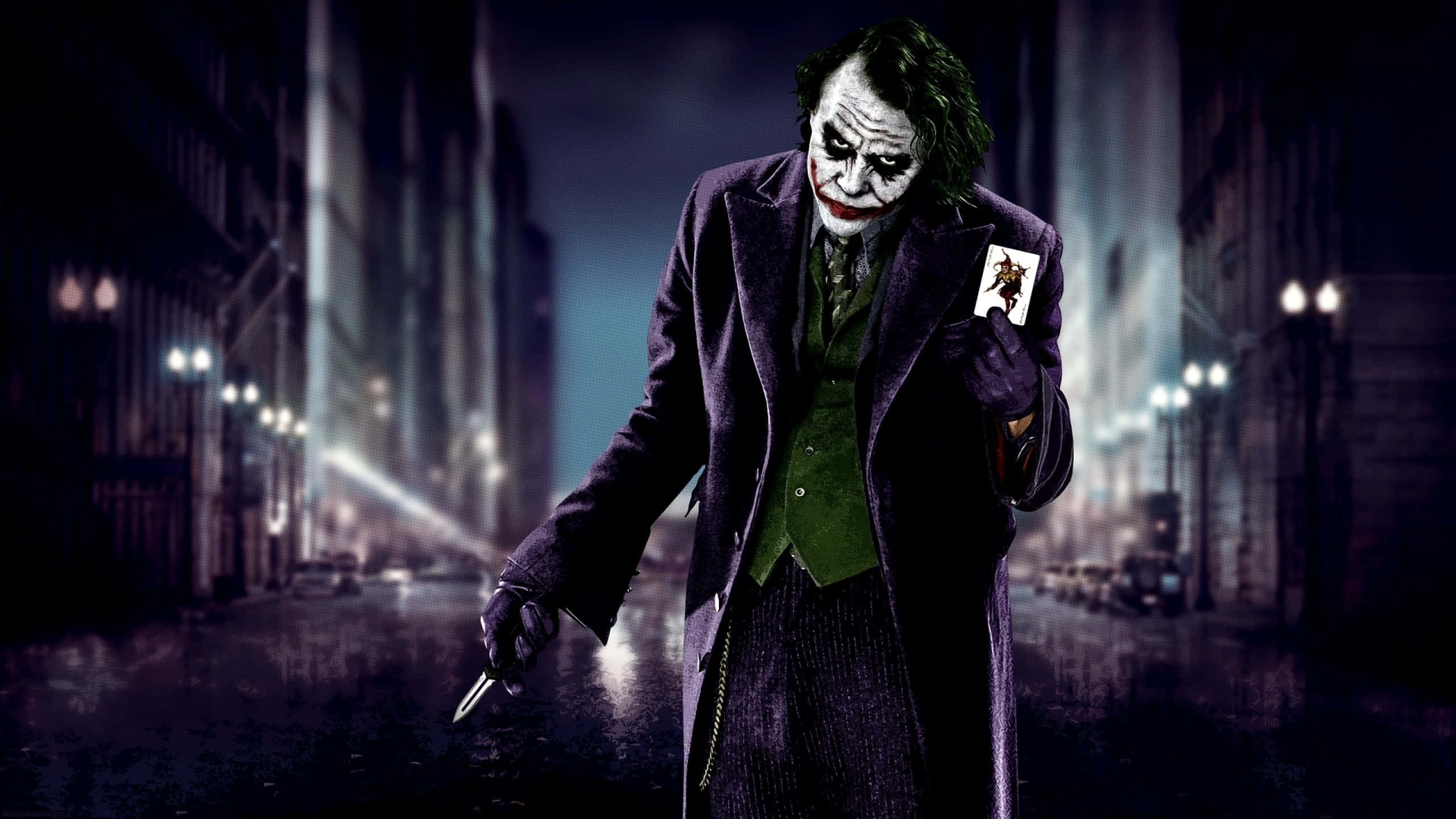 Dark Joker 桌布 壁紙 — 小丑在夜間哥譚市濕透的街道上，在閃爍的路燈下威脅性地站著，手持一張撲克牌和一把刀。