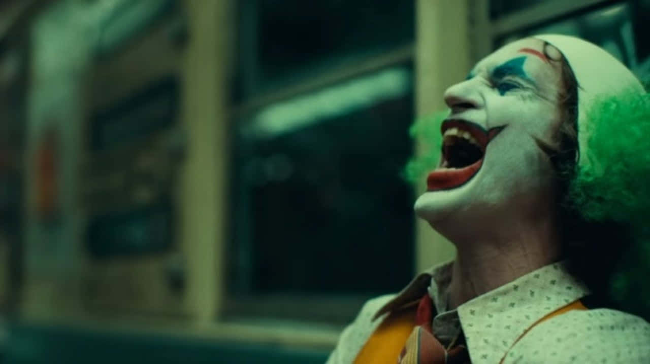 Joker Laughing 桌布 壁紙 — 小丑在昏暗的城市環境中狂笑的特寫，綠髮白臉。