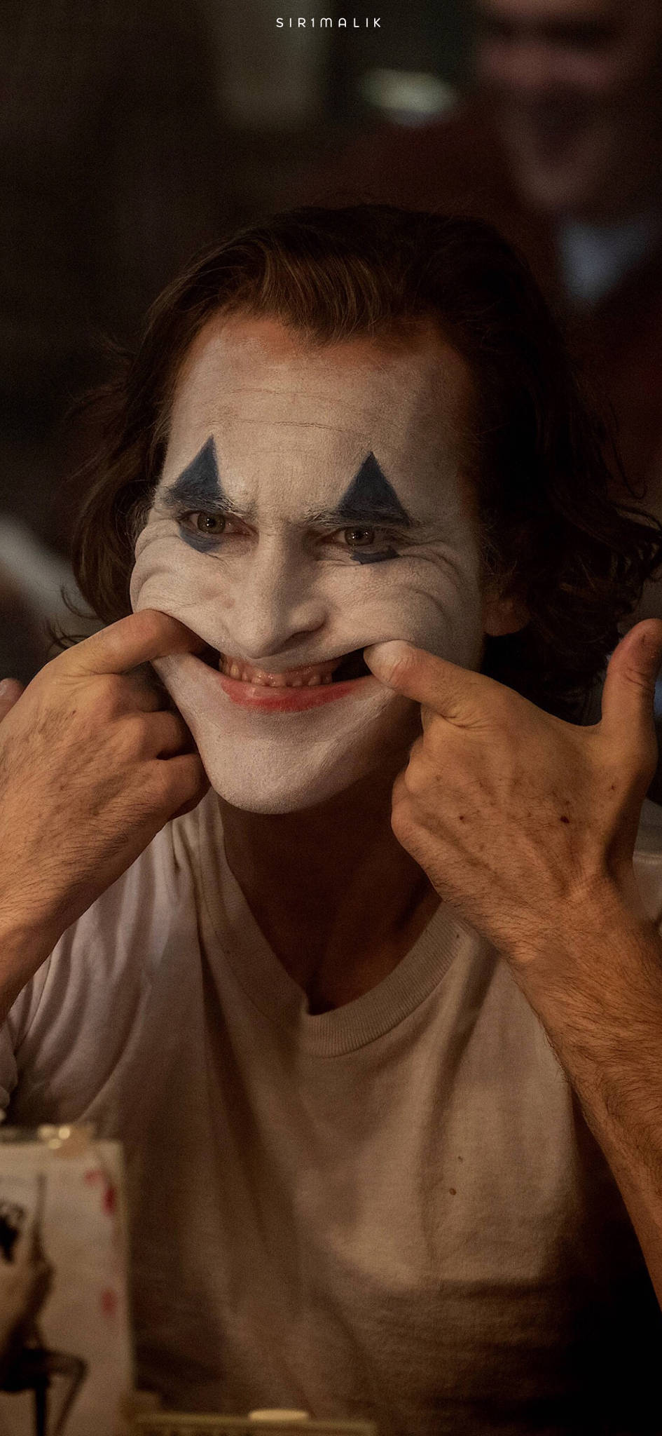 Joker 2019 桌布 壁紙 — 小丑在昏暗的房間中用雙手拉開塗上油漆的笑容的特寫。
