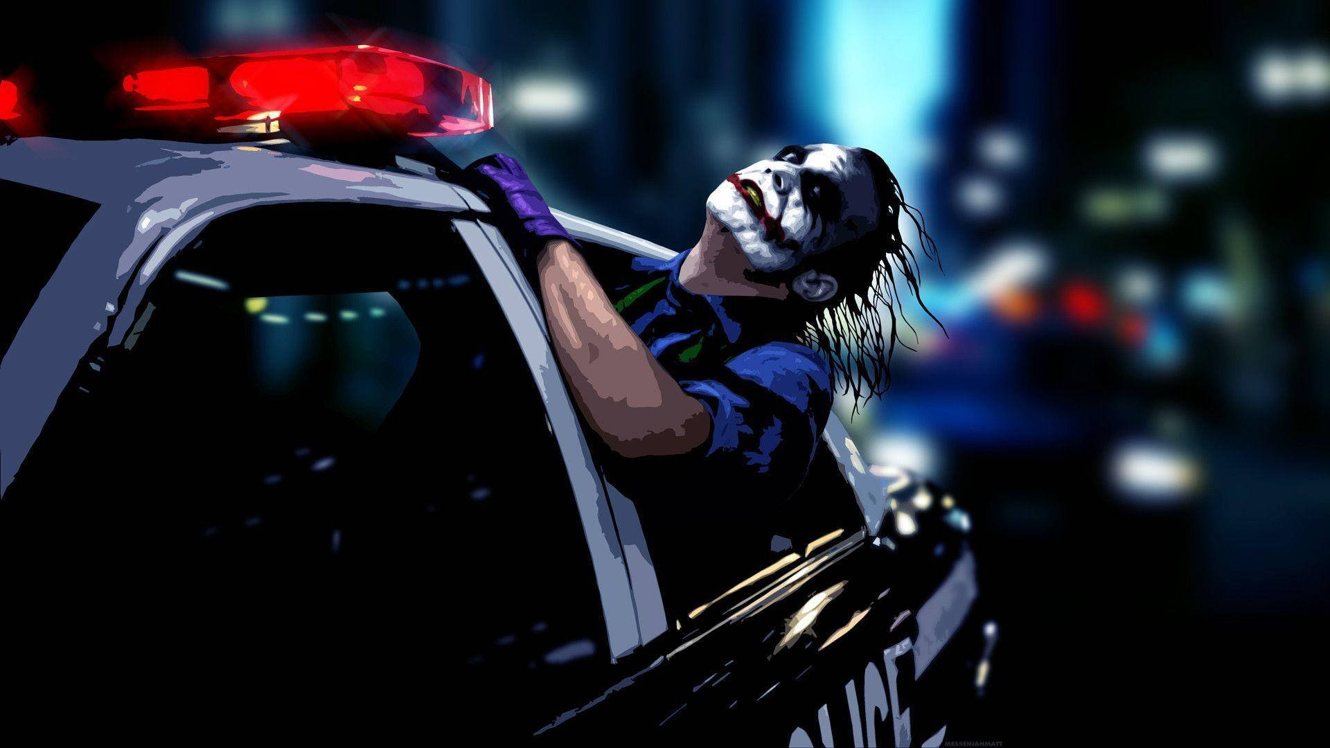 桌布 壁紙 — 小丑從一輛警車中探出頭來，紅色警燈在模糊的城市夜景背景下閃爍。