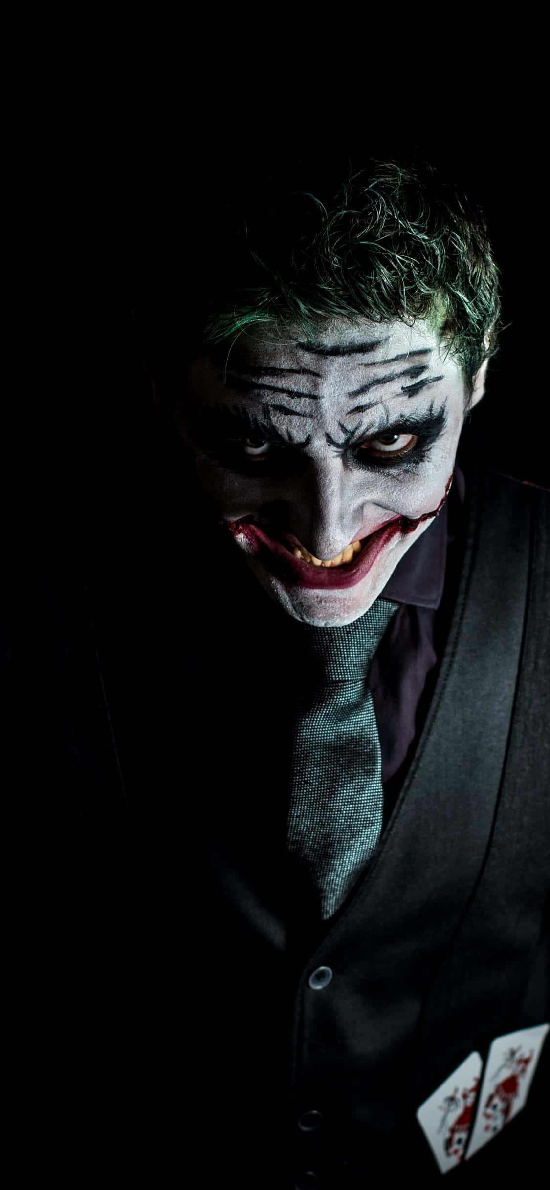 Dark Joker 桌布 壁紙 — 小丑的近距離特寫，臉上塗著白色顏料、紅唇和綠髮，背景為黑色，充滿威脅感。