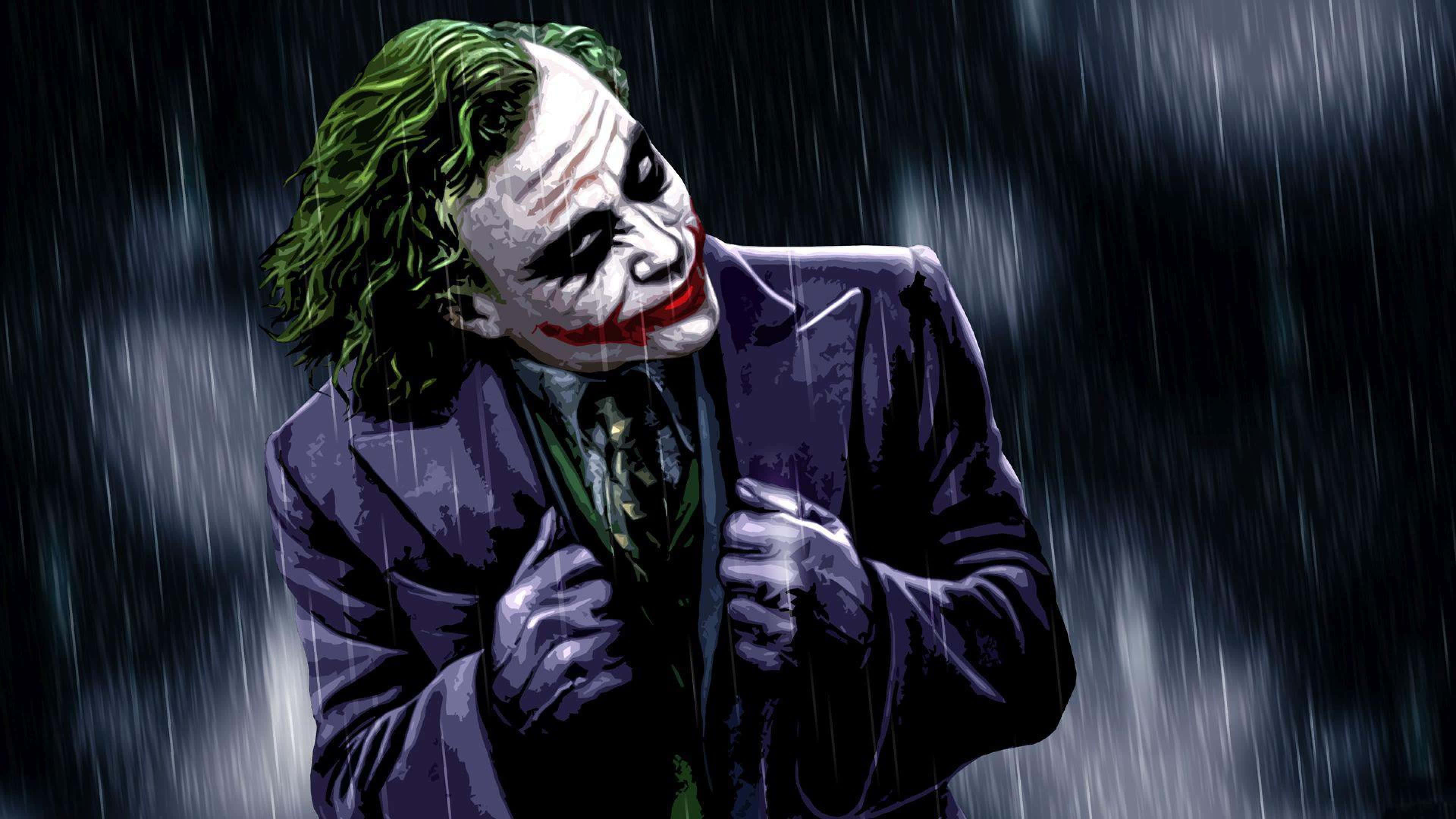Dark Knight Joker In 4K Ultra HD 桌布 壁紙 — 小丑站在傾盆大雨中，他的綠色頭髮和塗上的笑容在黑暗的暴風雨背景下顯得格外突出。