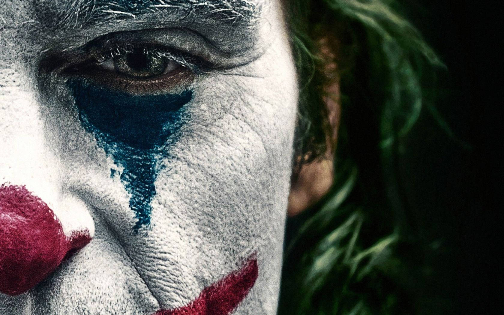 Joker 2019 桌布 壁紙 — 小丑臉部特寫，白色化妝、藍色眼淚、紅色嘴唇和綠色頭髮，背景深色。