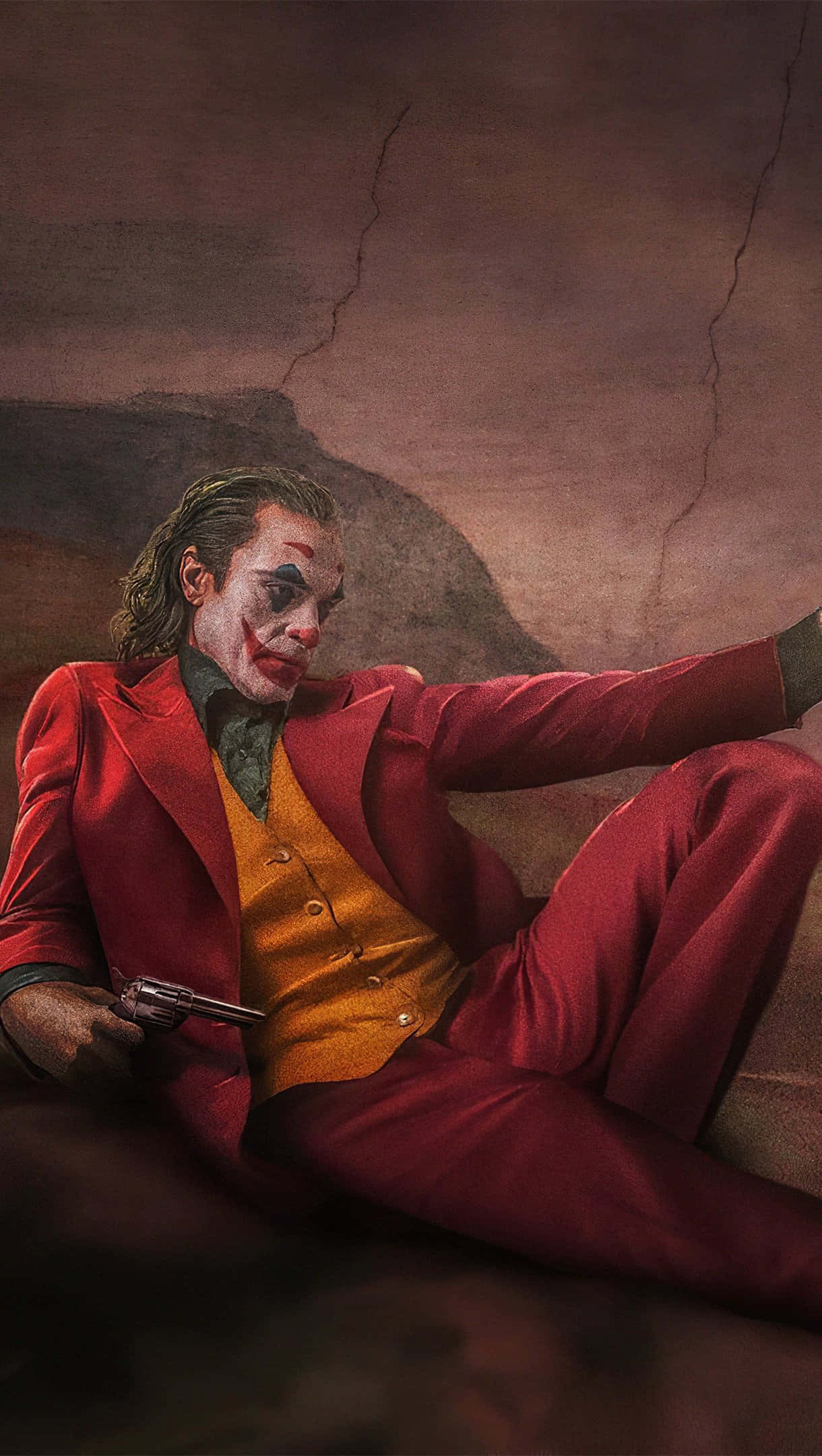 小丑 桌布 壁紙 — 小丑身穿紅色西裝，手持槍枝，隨意地坐在龜裂的大地背景前。