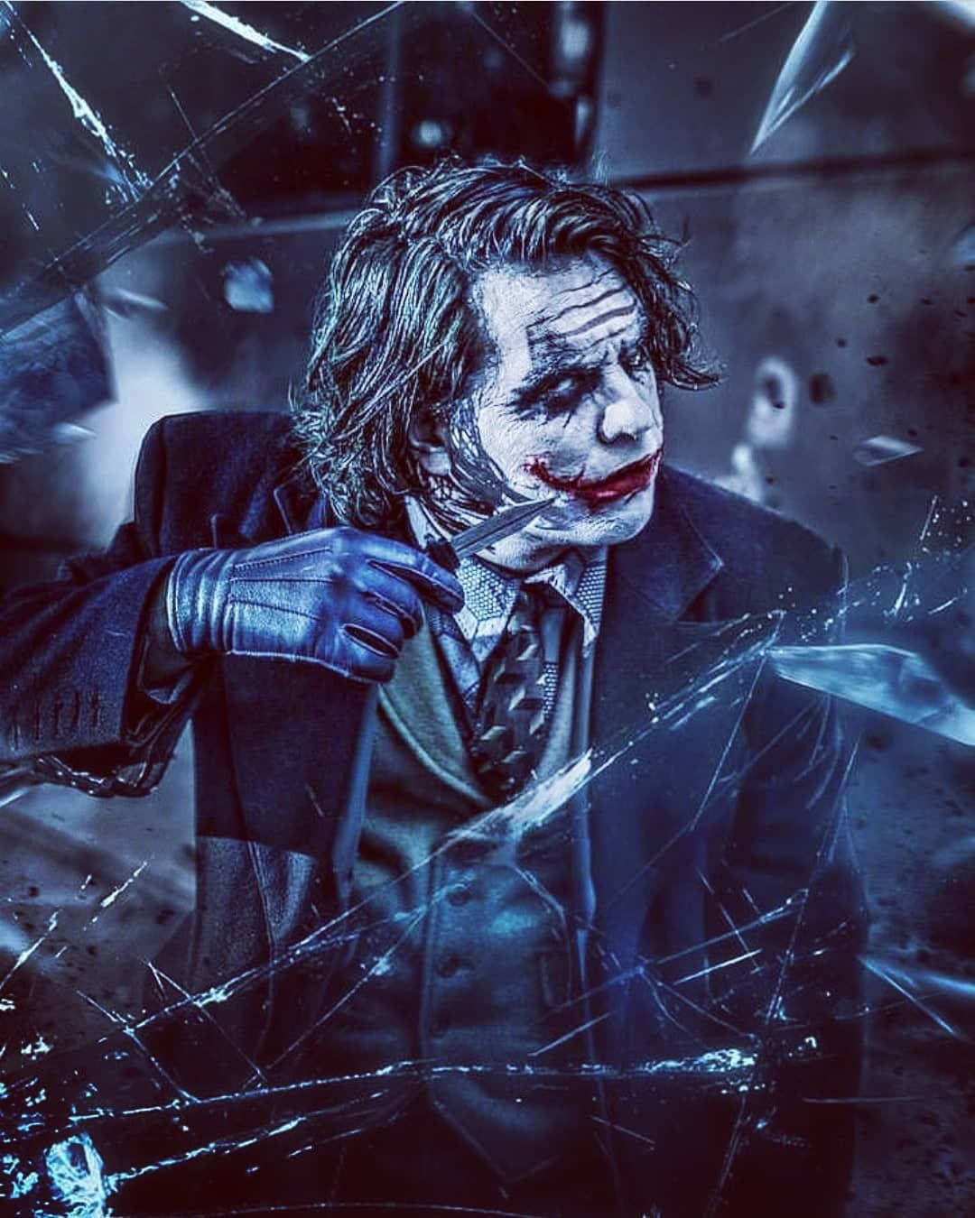 Why So Serious Joker 桌布 壁紙 — 小丑透過碎裂的玻璃冷笑，同時將刀架在自己脖子上，場景籠罩在冰冷的藍光中。