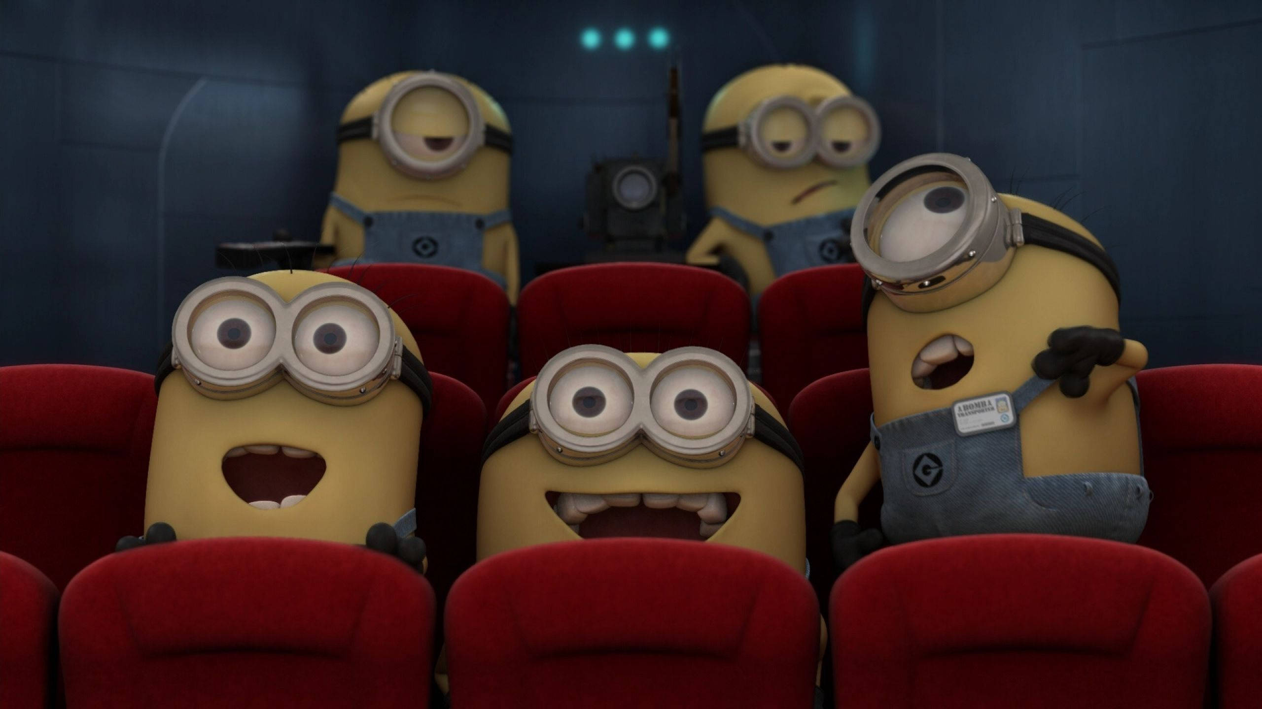Despicable Me 2 桌布 壁紙 — 小小兵坐在紅色戲院座位上，睜大眼睛，帶著喜悅的表情看電影。