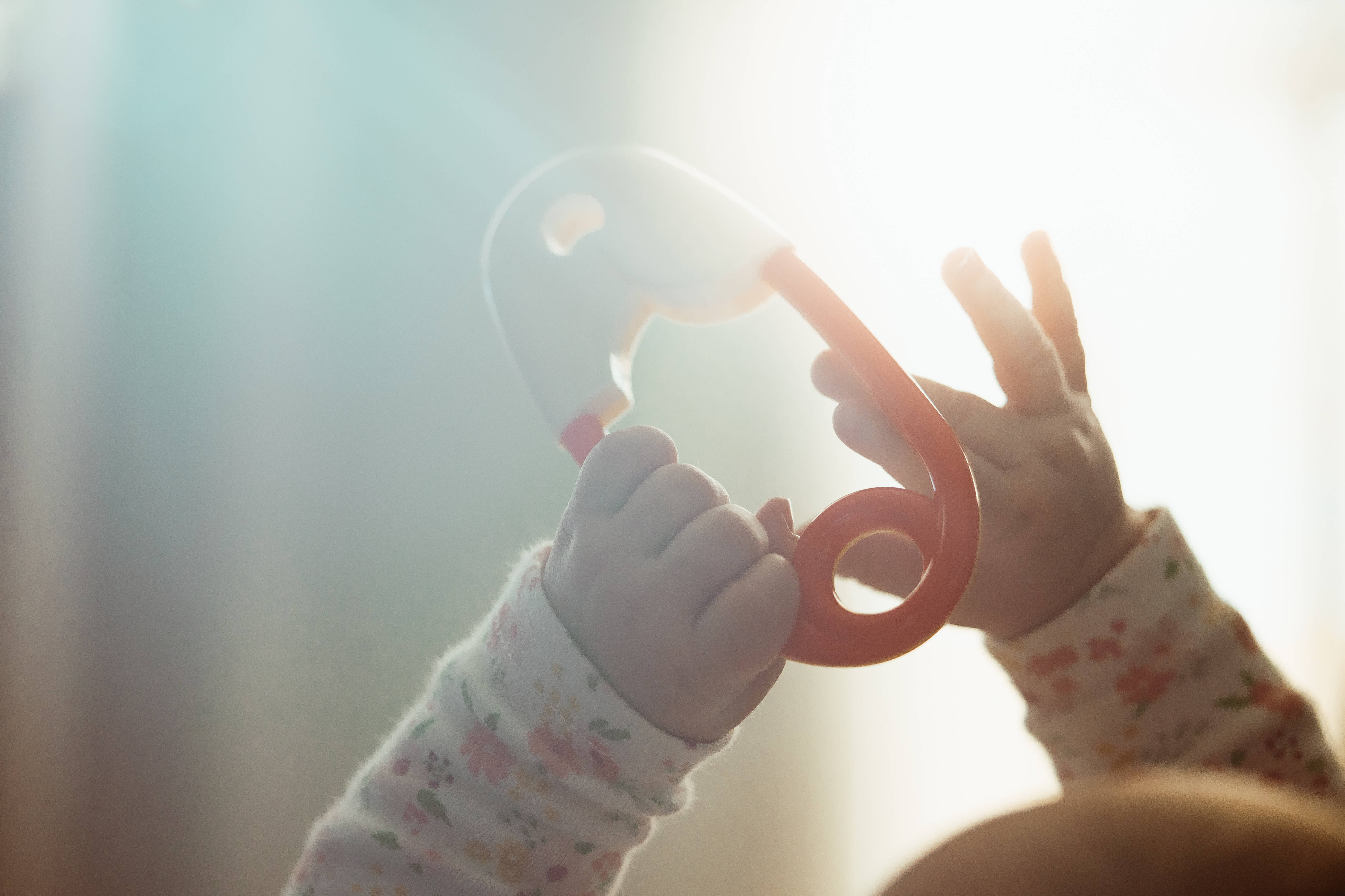 Baby HD 桌布 壁紙 — 小手握著紅色固齒器，映襯著陽光普照的窗戶，配以柔軟的花袖。