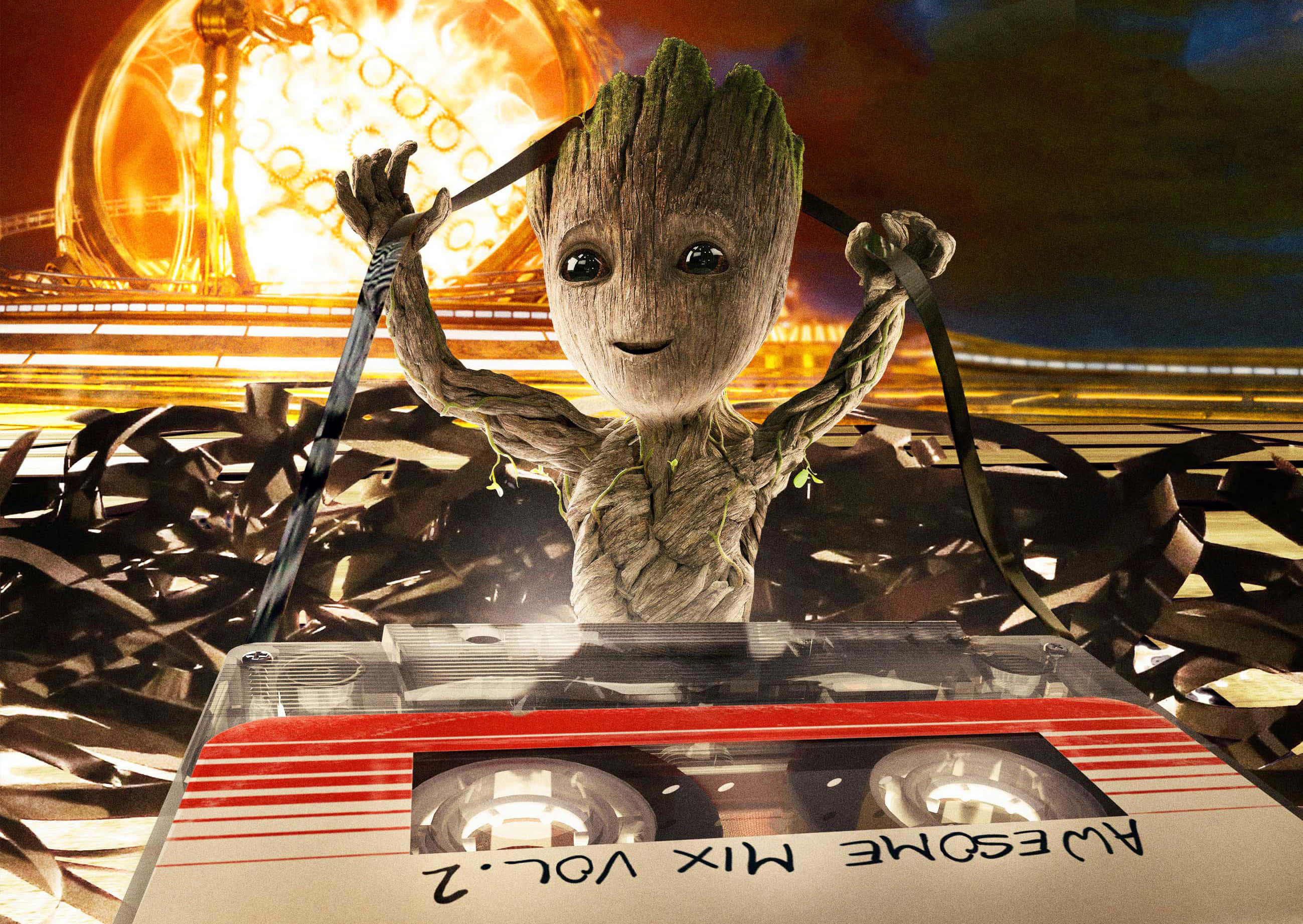Guardians Of The Galaxy 2 桌布 壁紙 — 小格魯特在發光的金色球體背景下，開心地舉著卡式錄音帶的帶絲，下方是標有 'Awesome Mix Vol. 2' 的卡帶。