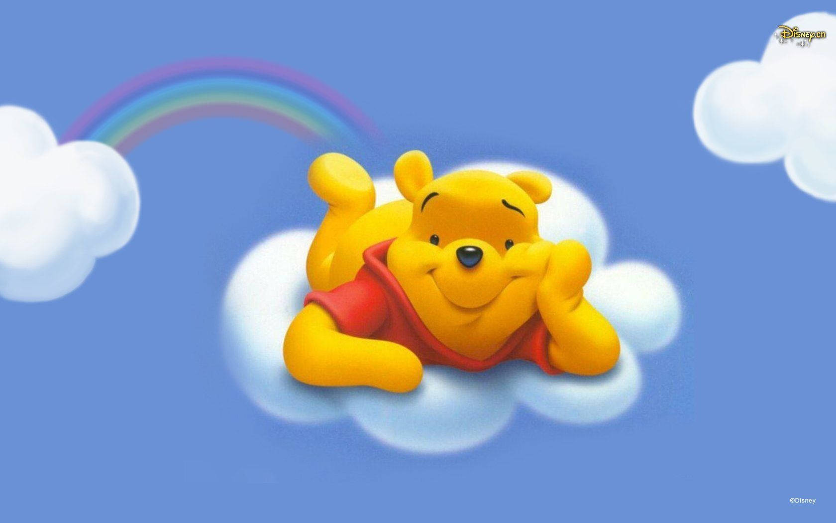 Disney Winnie The Pooh 桌布 壁紙 — 小熊維尼在晴朗的藍天下，在一條色彩繽紛的彩虹下面，開心地躺在柔軟的雲朵上。