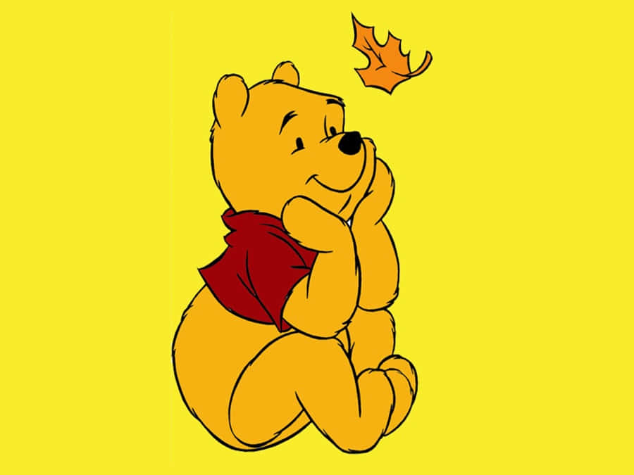 winnie the pooh 桌布 壁紙 — 小熊維尼坐在明亮的黃色田野中沉思，一片橙色樹葉漂浮在他上方。