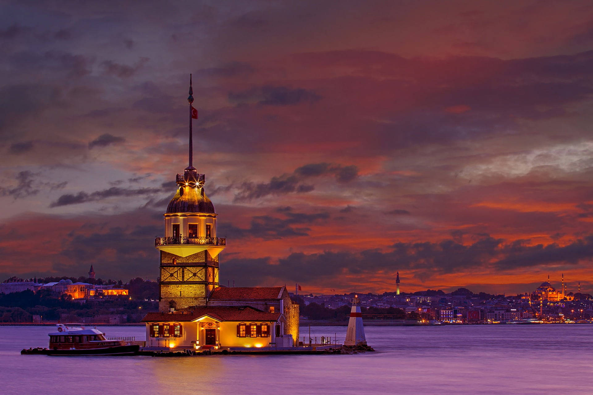Istanbul 桌布 壁紙 — 少女塔在伊斯坦堡水道上的火紅日落天空下溫暖地發光，遠處的城市燈光閃爍。