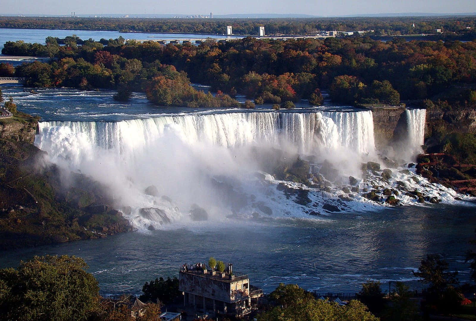 720p Niagara Falls 桌布 壁紙 — 尼亞加拉大瀑布全景，強力傾瀉入霧氣瀰漫的河流，周圍環繞著秋色樹木。