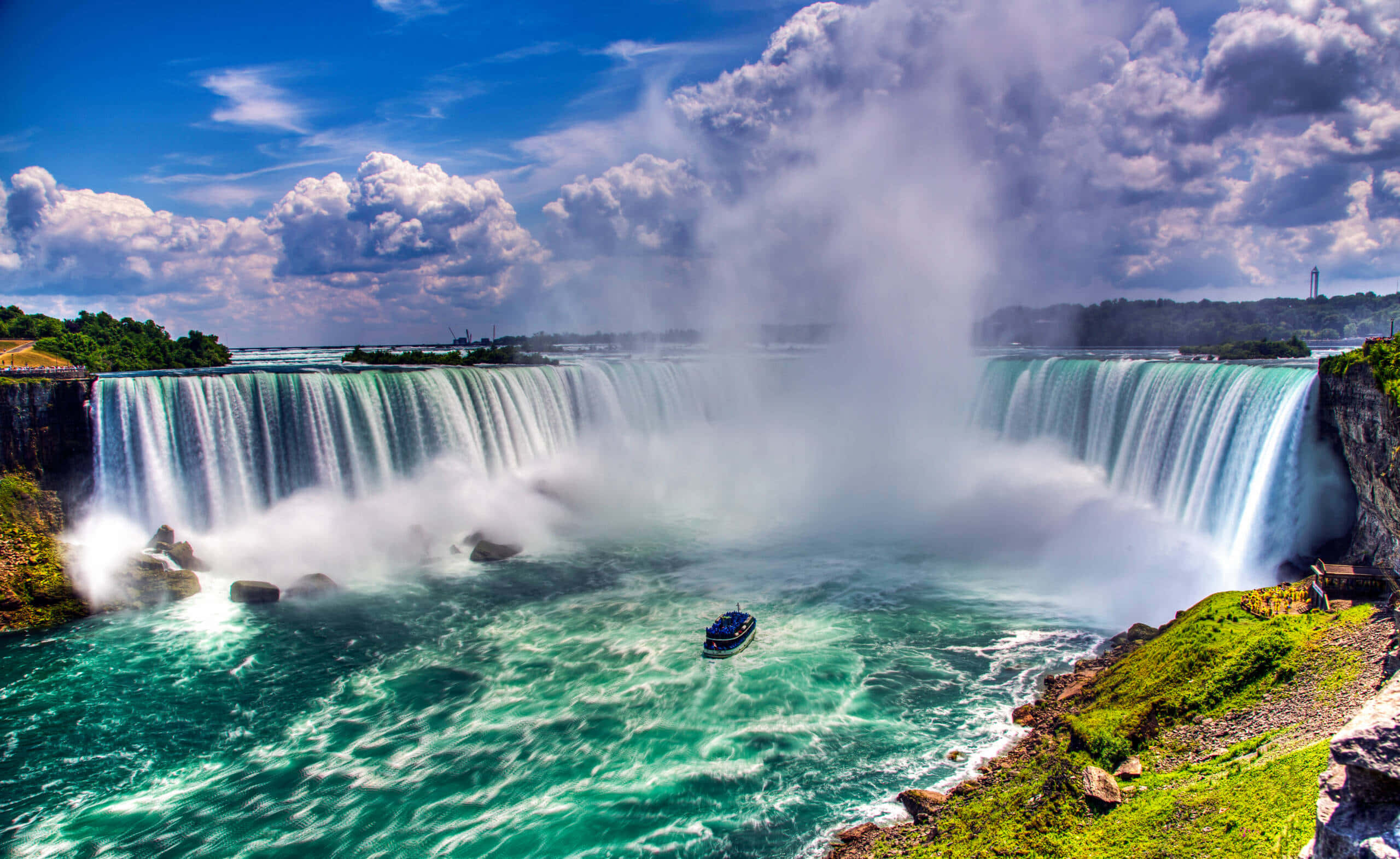 Niagara Falls 桌布 壁紙 — 尼亞加拉大瀑布在戲劇性的多雲天空下，雄偉地傾瀉入碧綠水中的廣角景觀。