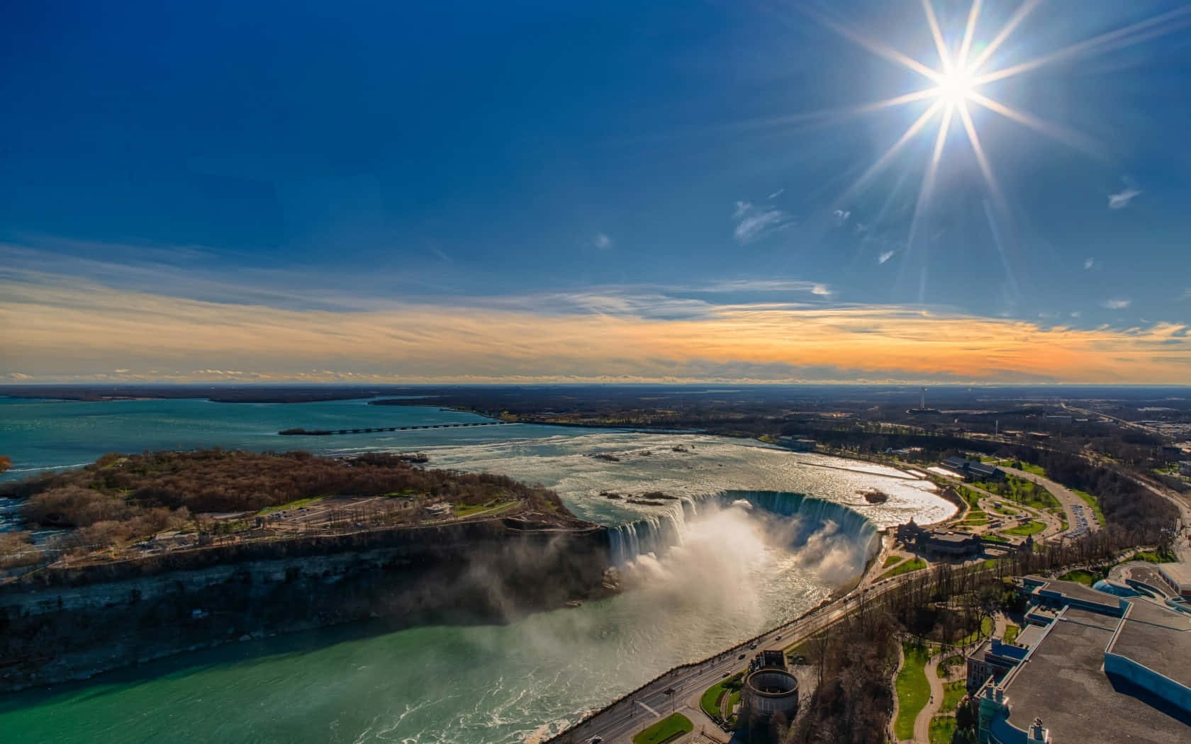 720p Niagara Falls 桌布 壁紙 — 尼亞加拉大瀑布在燦爛陽光下傾瀉而下的空拍圖，伴隨著金色雲彩和碧綠海水。