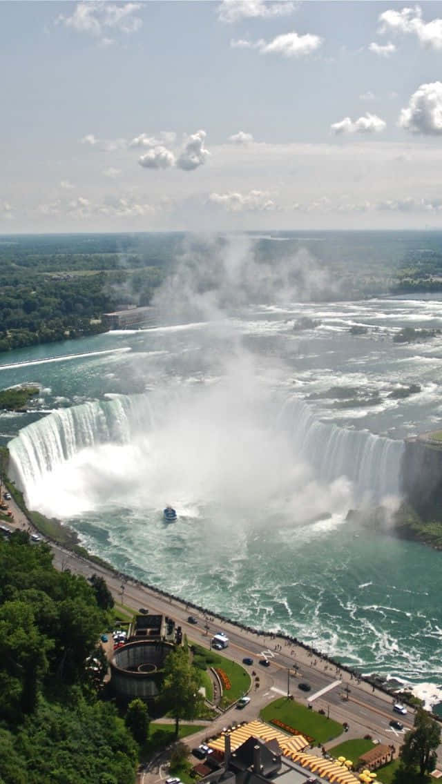 Niagara Falls Canada 桌布 壁紙 — 尼亞加拉大瀑布從高空俯瞰，強勁地傾瀉入霧氣瀰漫的河流，一艘觀光船在下方湍急的水域中航行。