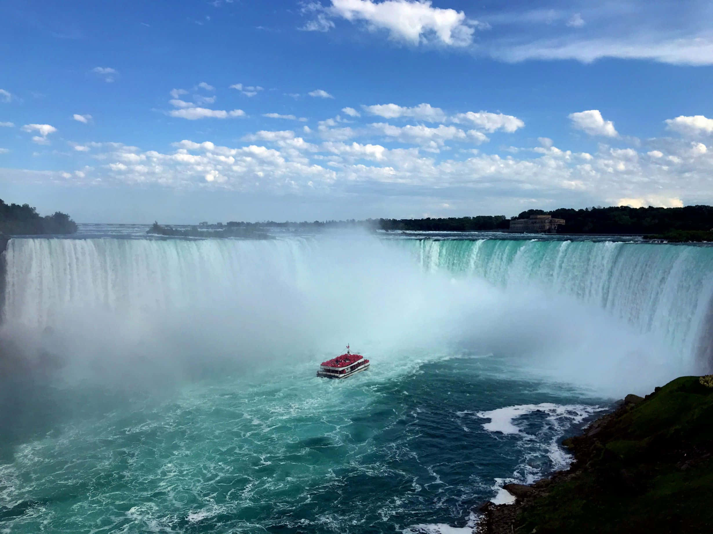 Niagara Falls 桌布 壁紙 — 尼亞加拉大瀑布的壯麗廣角景觀，一艘紅色觀光船在瀑布傾瀉而下的霧氣下方，航行於湍急的碧綠水域中。