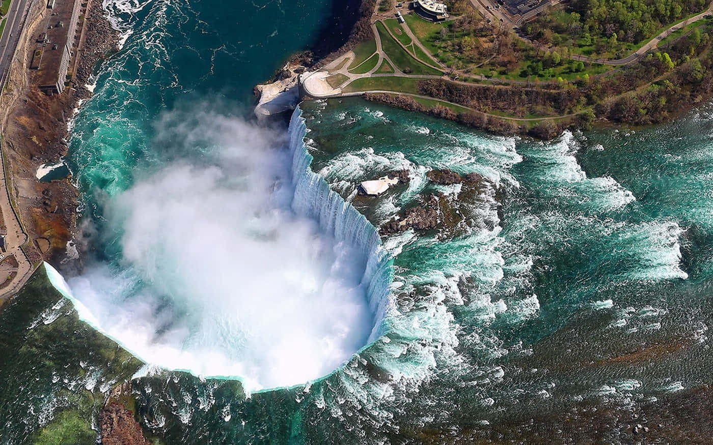 720p Niagara Falls 桌布 壁紙 — 尼亞加拉大瀑布的鳥瞰圖，瀑布傾瀉入一個霧氣瀰漫的盆地，四周環繞著茂密的綠植和蜿蜒的小徑。