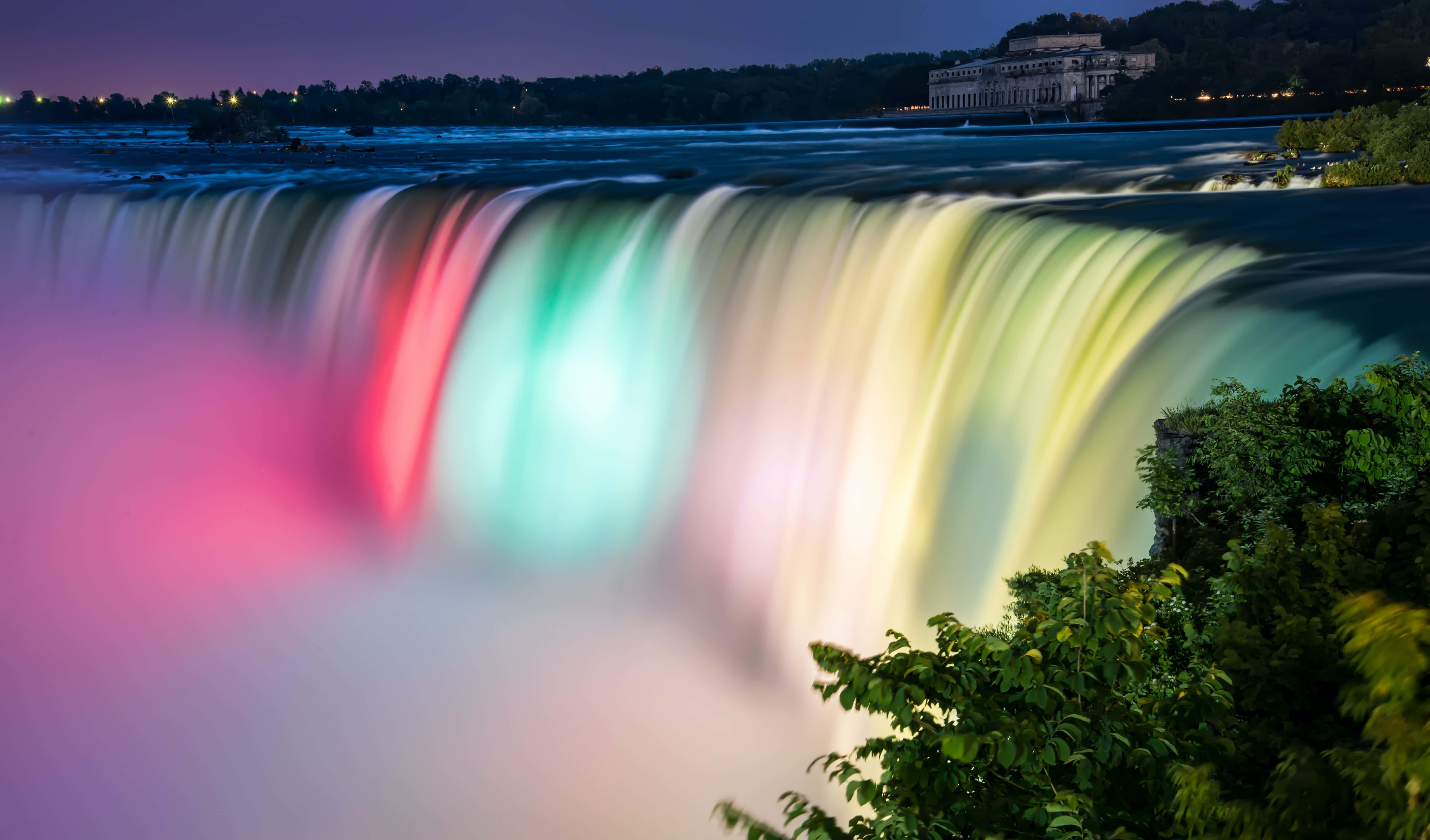 Waterfalls 桌布 壁紙 — 尼亞加拉瀑布在夜間被鮮豔的彩虹燈光照亮，水流在霧氣中傾瀉而下，背景是黑暗的天空。