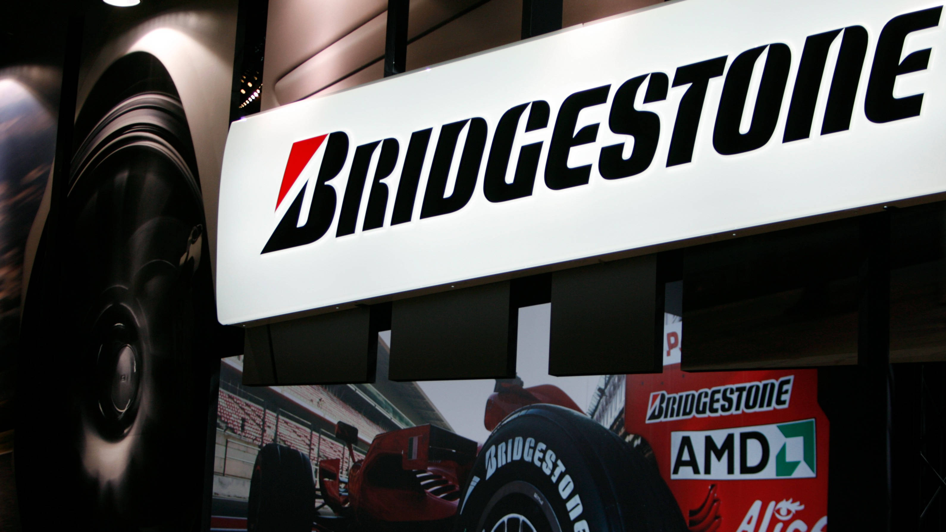標誌 桌布 壁紙 — 展示廳環境中，Bridgestone 標誌與賽車輪胎及一級方程式賽車背景的特寫。