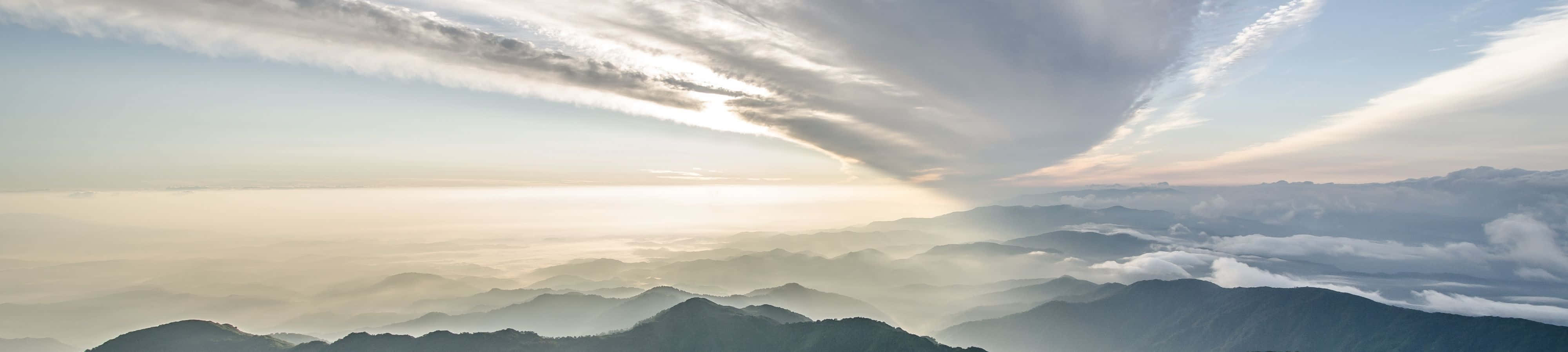 4K 自然 桌布 壁紙 — 層層山脈從雲海中浮現的 panoramic 景觀，日出時柔和的金色光芒穿透上方縷縷雲層。