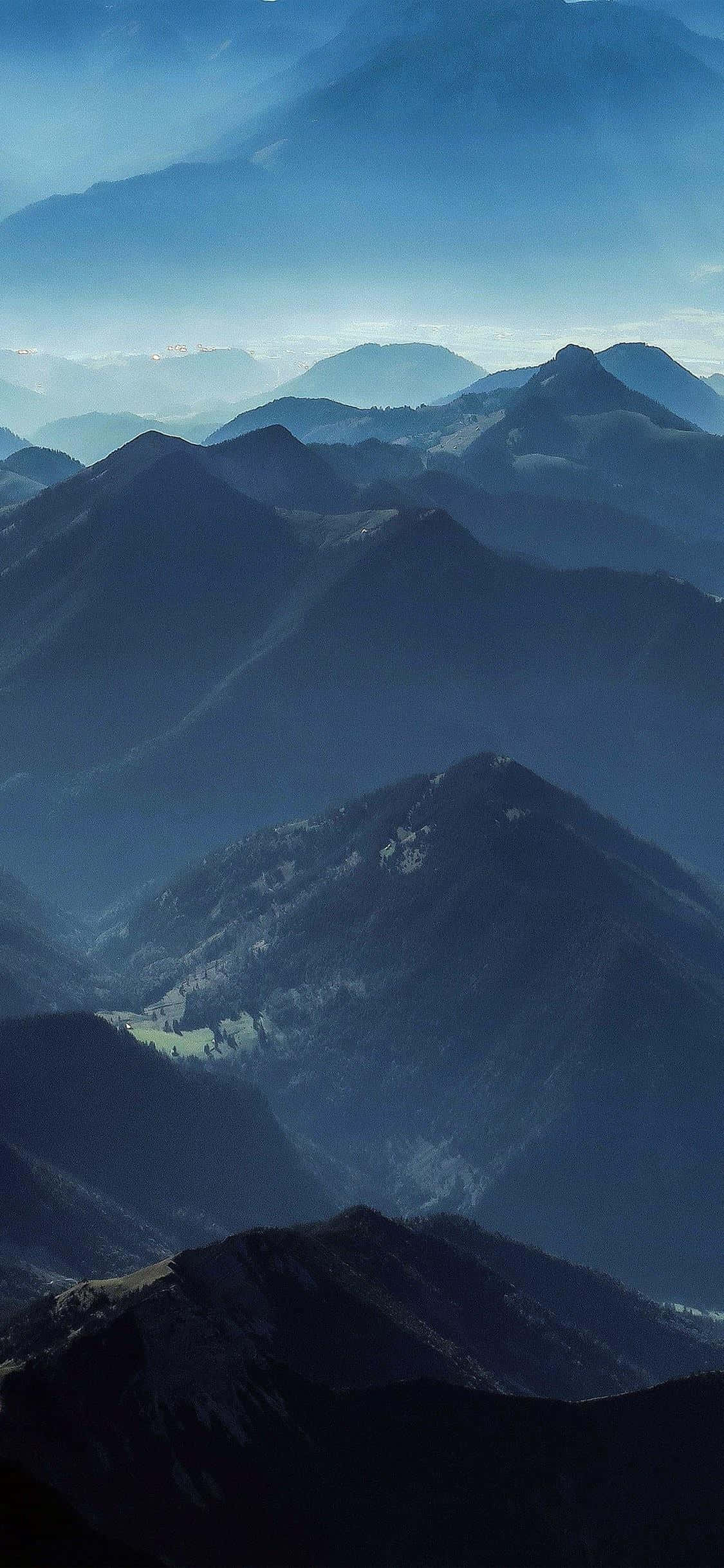 iPhone X Nature 桌布 壁紙 — 層層疊疊的山峰在柔和晨光下逐漸融入大氣藍色的薄霧中。