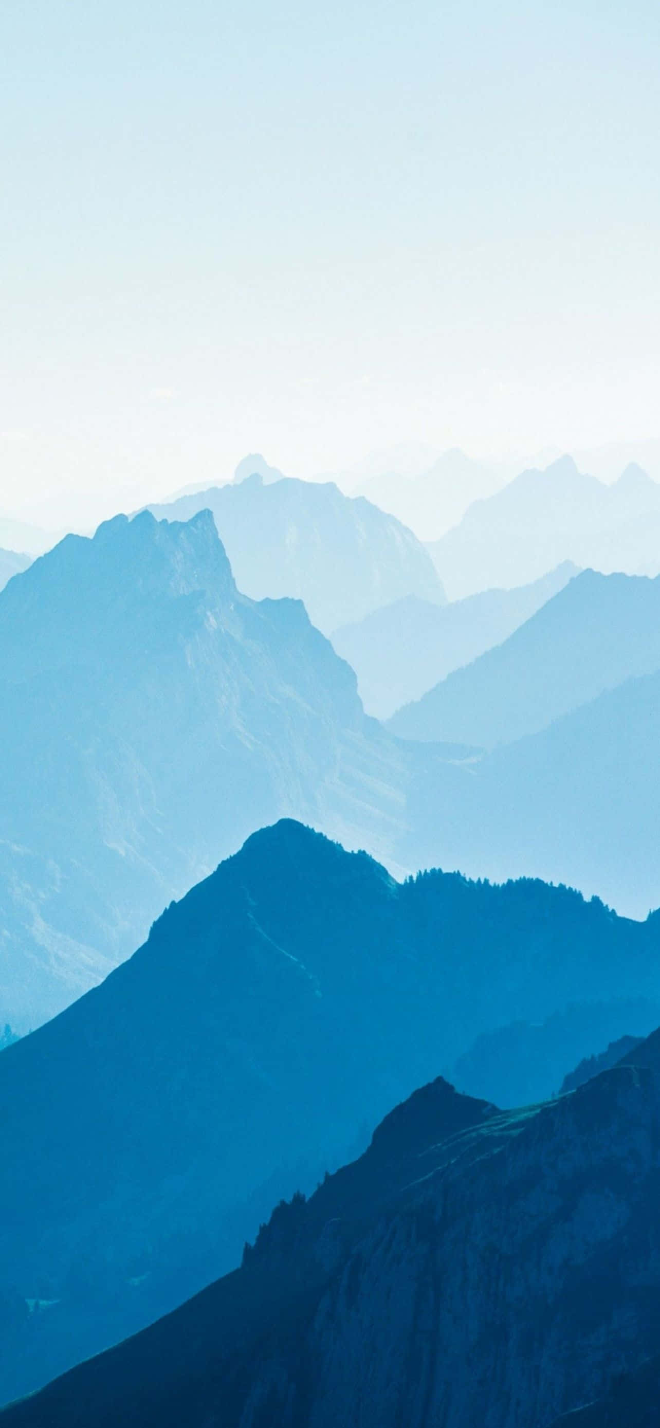 Mountain iPhone 桌布 壁紙 — 層層疊疊的山峰在蒼白的天空下逐漸融入迷濛的藍色薄霧中。