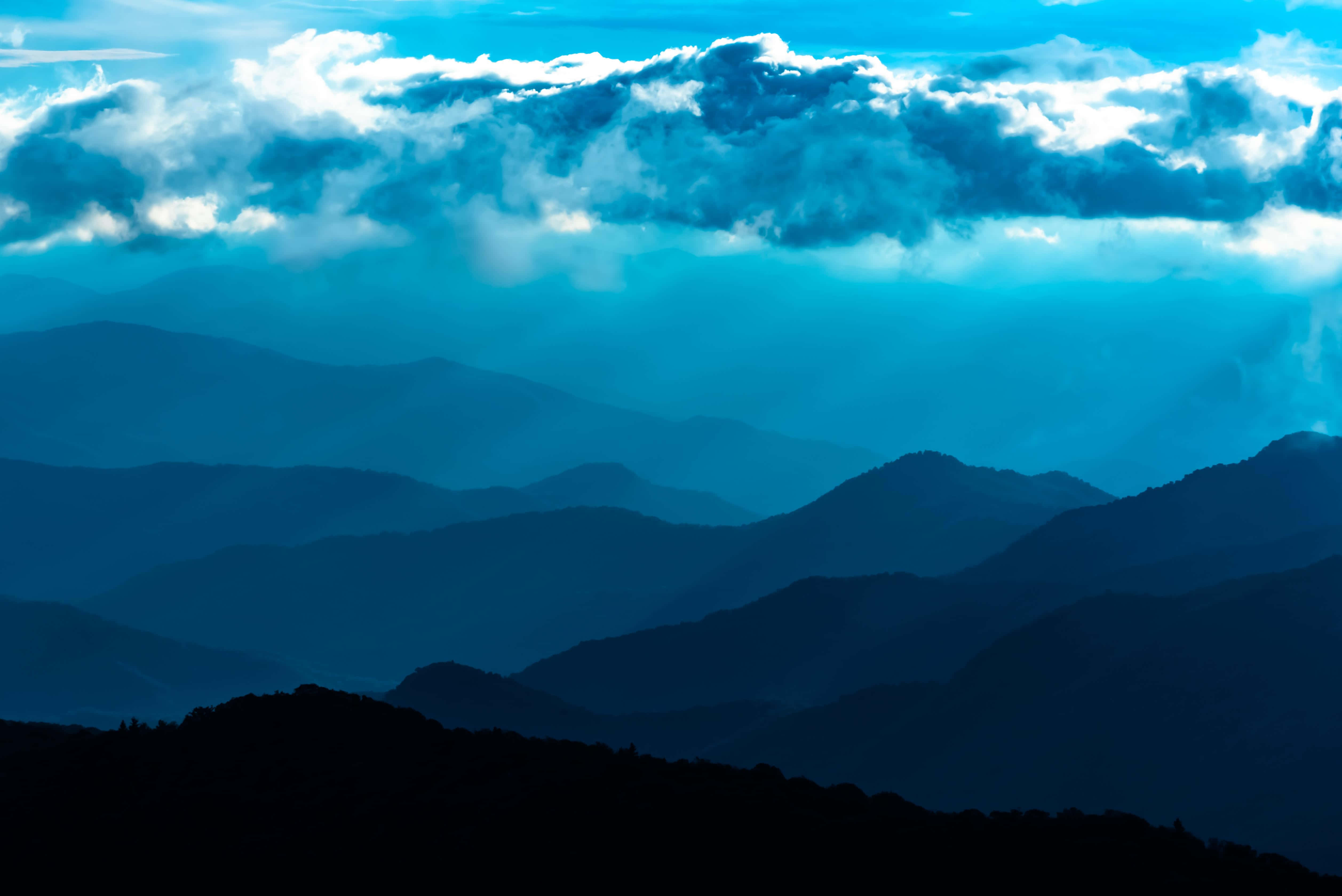 Blue Ridge Mountains 桌布 壁紙 — 層層疊疊的山脈在戲劇性的多雲天空下，逐漸融入大氣藍色的薄霧中。