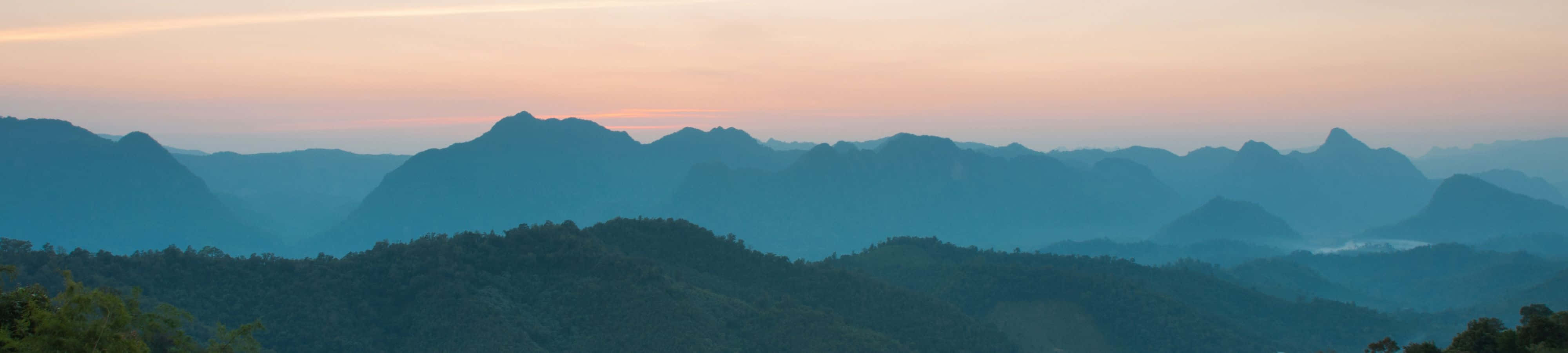 4K 自然 桌布 壁紙 — 層層疊疊的山脈在柔和粉紅與橙色的日出天空下逐漸消失在霧中。