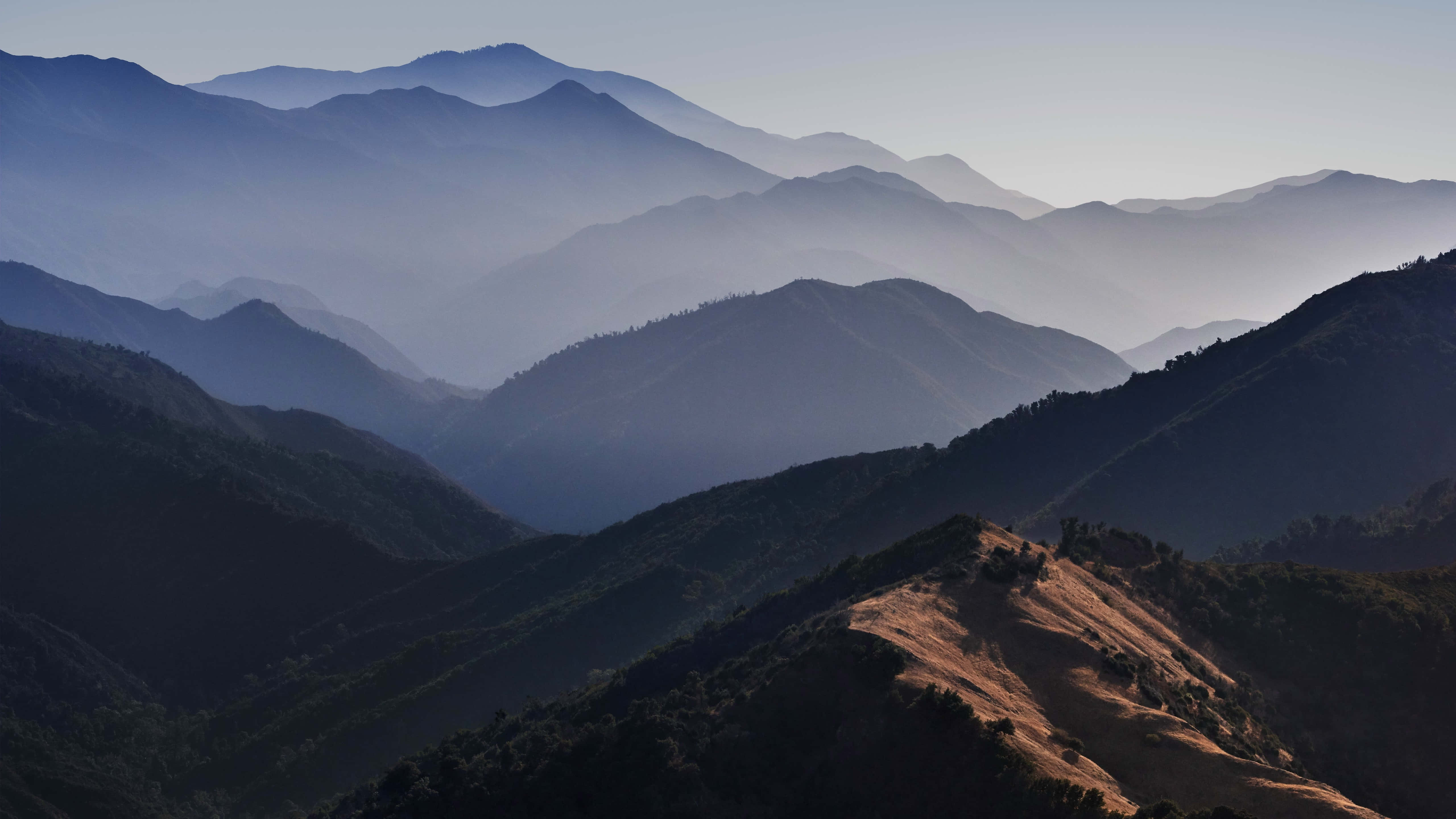 macOS 桌布 壁紙 — 層層疊疊的山脊在柔和晨光下逐漸消失在迷濛的藍色遠方。