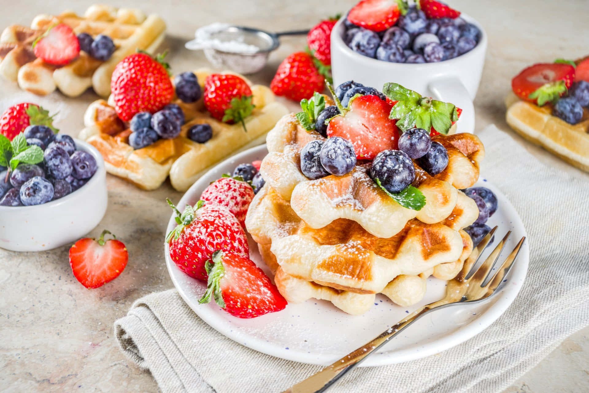 Waffle 桌布 壁紙 — 層層疊起的金黃色鬆餅，上面鋪上新鮮草莓、藍莓和薄荷葉，撒上糖粉。
