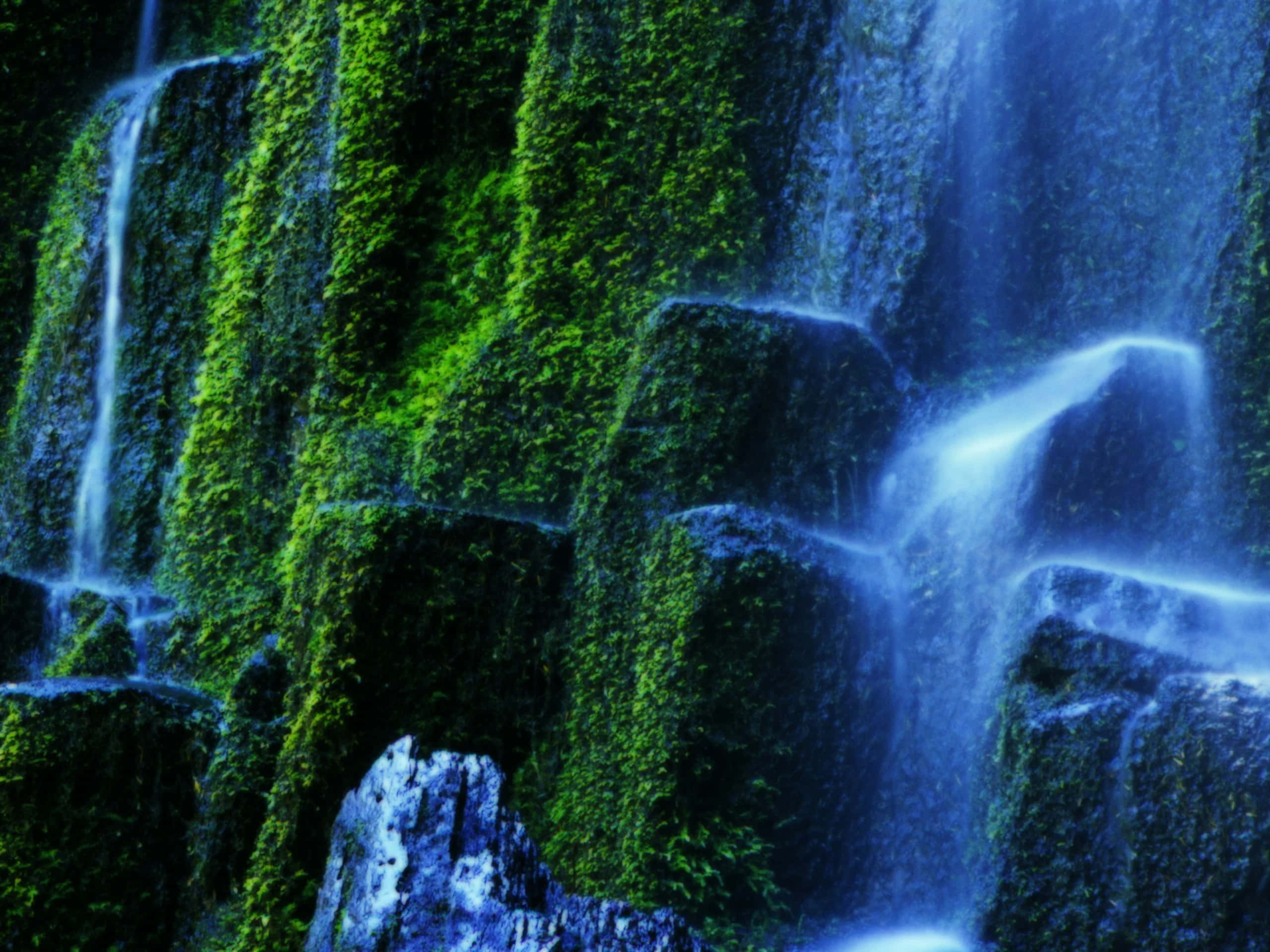 3d Waterfall 桌布 壁紙 — 層疊的瀑布流過長滿苔蘚的岩石，岩石散發出充滿活力的綠色和涼爽的藍色光芒。