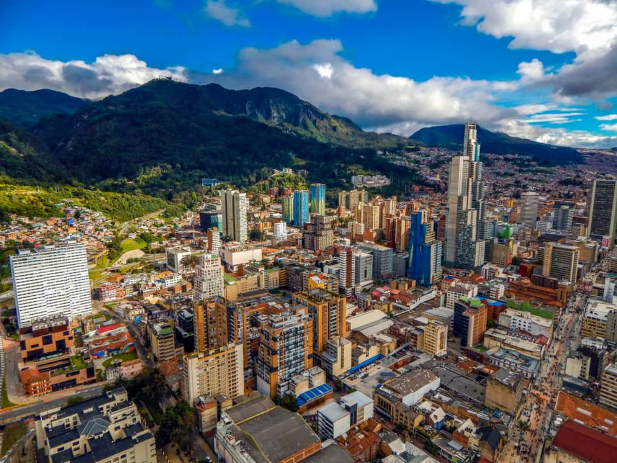 Colombia 桌布 壁紙 — 山谷中充滿活力的城市的鳥瞰圖，周圍是鬱鬱蔥蔥的綠色山脈，明亮的藍天上有蓬鬆的雲朵。